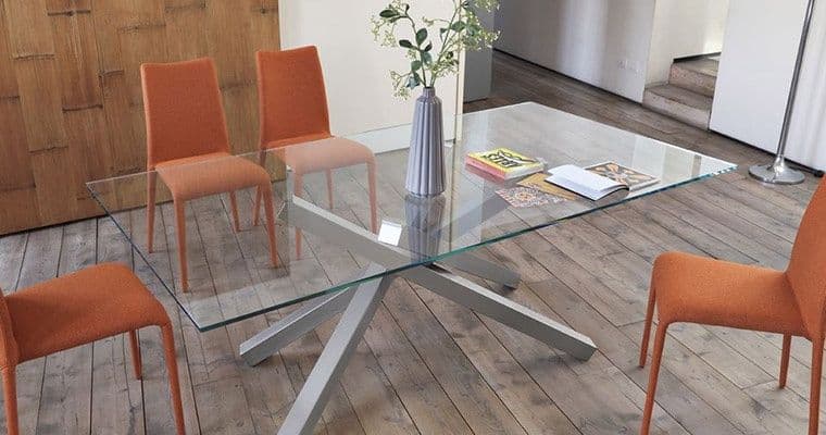 Contemporary glass dining table with a stylish design, featuring a custom glass top and a modern base, surrounded by orange chairs. Ideal for showcasing tempered glass craftsmanship.
