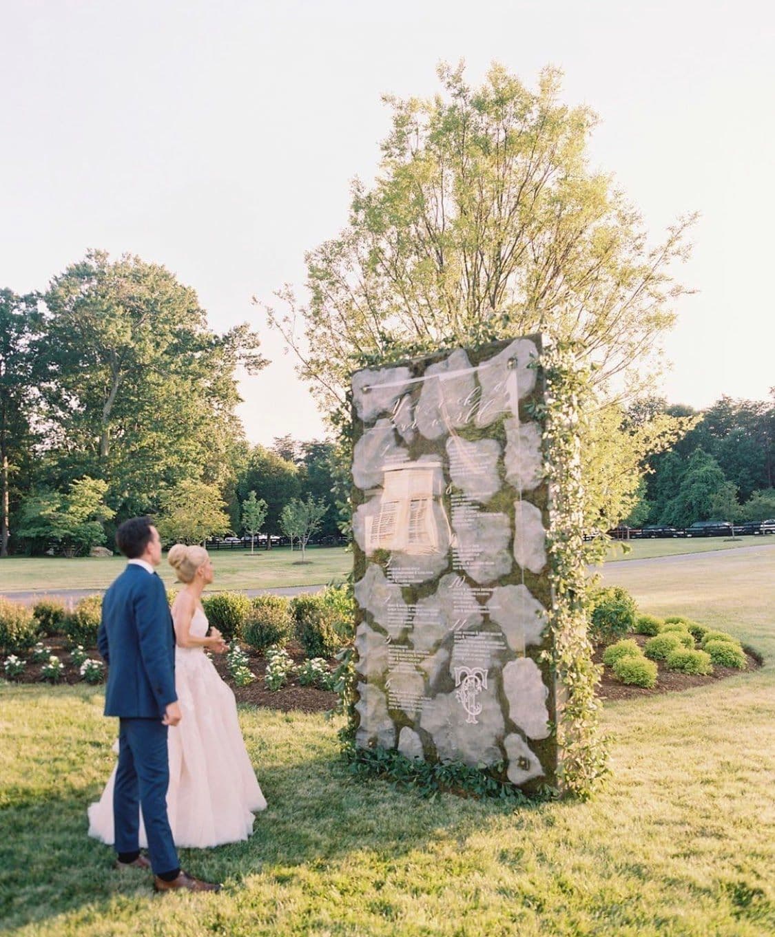 Couple admiring a unique glass installation surrounded by greenery, representing custom glass artistry, ideal for shower doors, table tops, and mirrors with tempered and beveled glass edges.