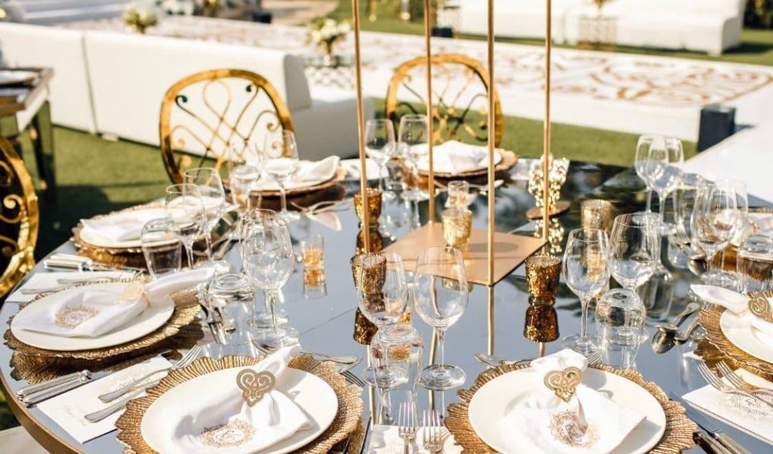 Elegant dining setup featuring a mirrored table top with gold accents, perfect for showcasing custom glass designs, including tempered and beveled glass edges, alongside beautifully arranged dinnerware and glassware.