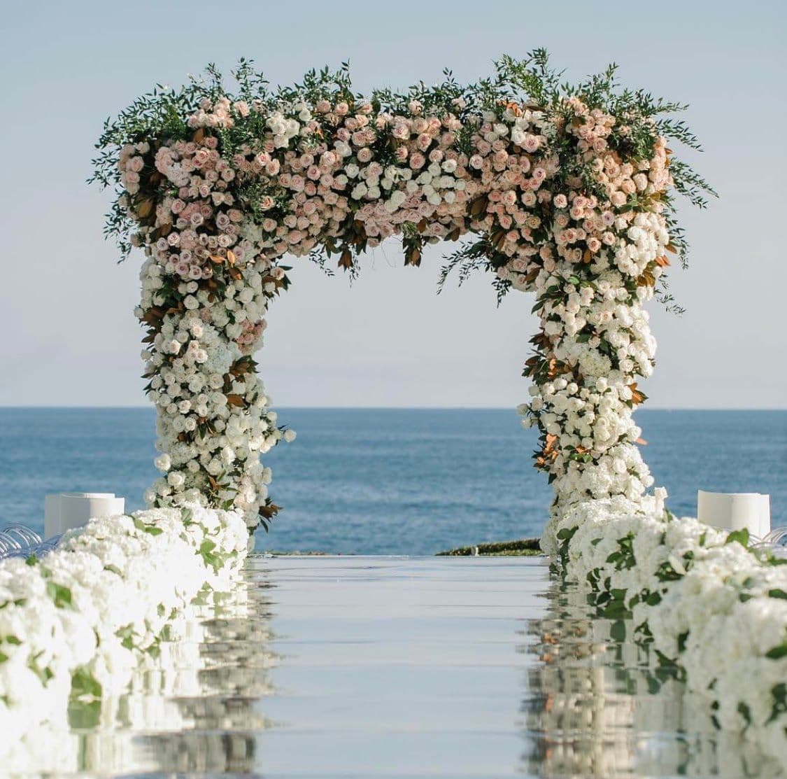 Elegant floral archway at a seaside wedding venue, showcasing a serene backdrop perfect for custom glass applications like shower doors and mirrors, emphasizing serene aesthetics with glass walkways.
