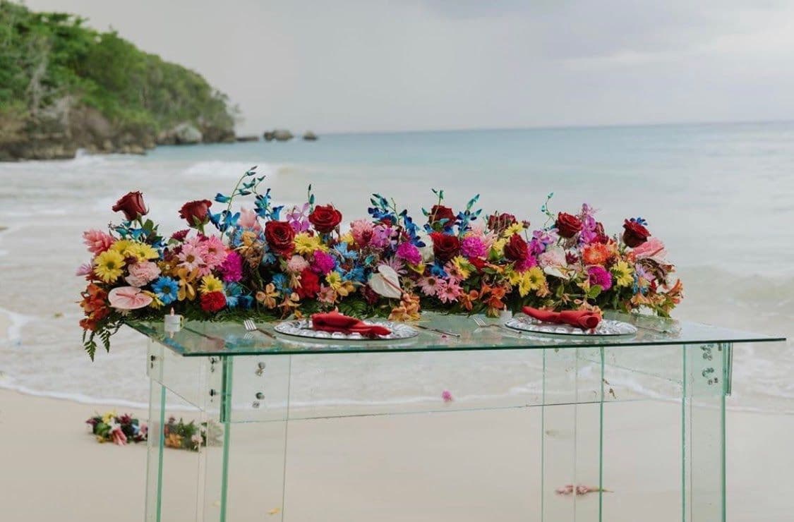 Elegant glass table adorned with vibrant flowers, showcasing custom glass design for unique events, ideal for table tops and decorative displays by the seaside.