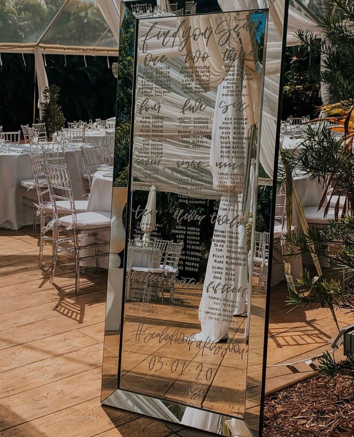 Custom beveled mirror displaying an elegant seating chart in a beautifully set event space, showcasing our expertise in decorative mirrors and custom glass solutions.