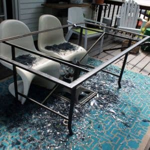 Broken glass table top with shattered tempered glass pieces scattered on a deck