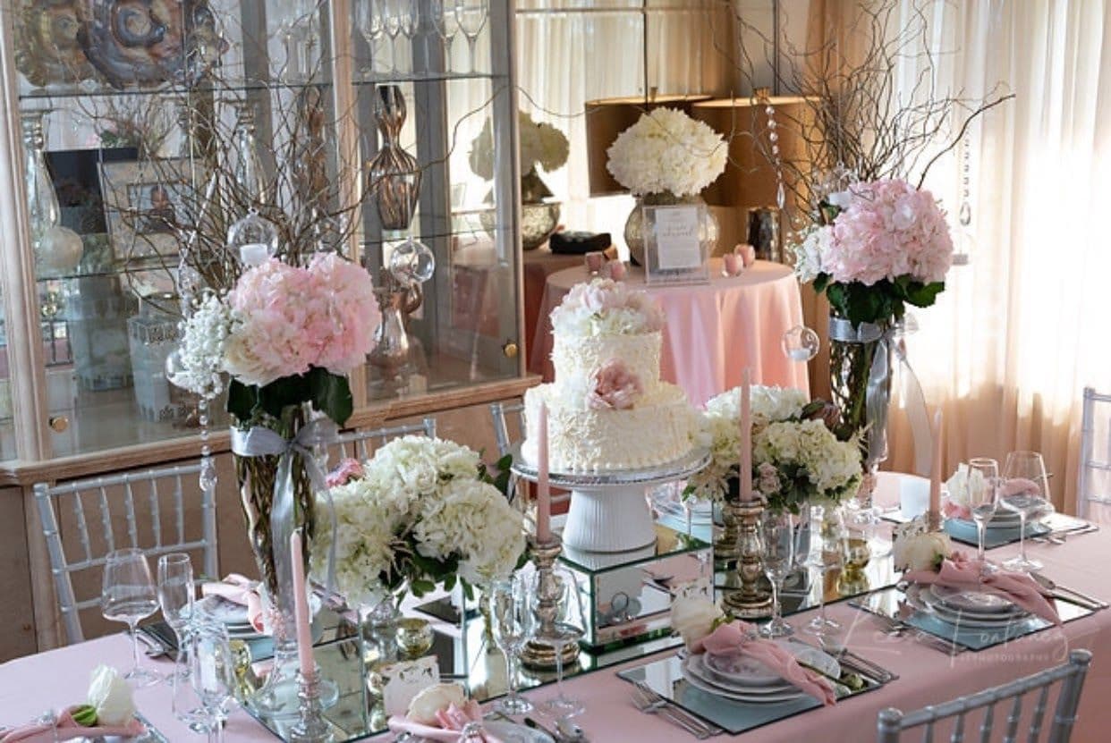 Elegant dining table adorned with floral arrangements, a wedding cake, and custom glass tabletops reflecting light, perfect for events featuring shower doors, mirrors, and beveled glass edge designs.