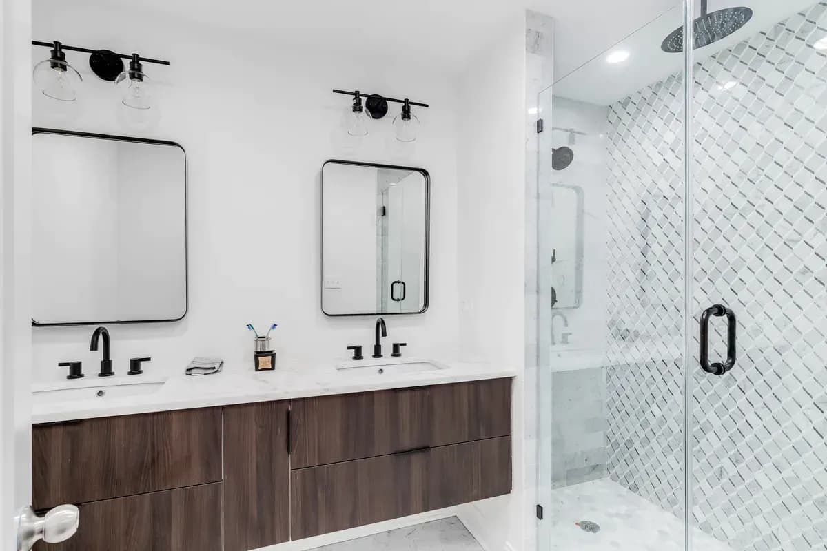 white bathroom with two rectangle mirrors with rounded edges and black frame with white granite sink and black hardware with wood shelving and white tile floor. Tile ground in shower with black hardware and diamond pattern tiled wall.