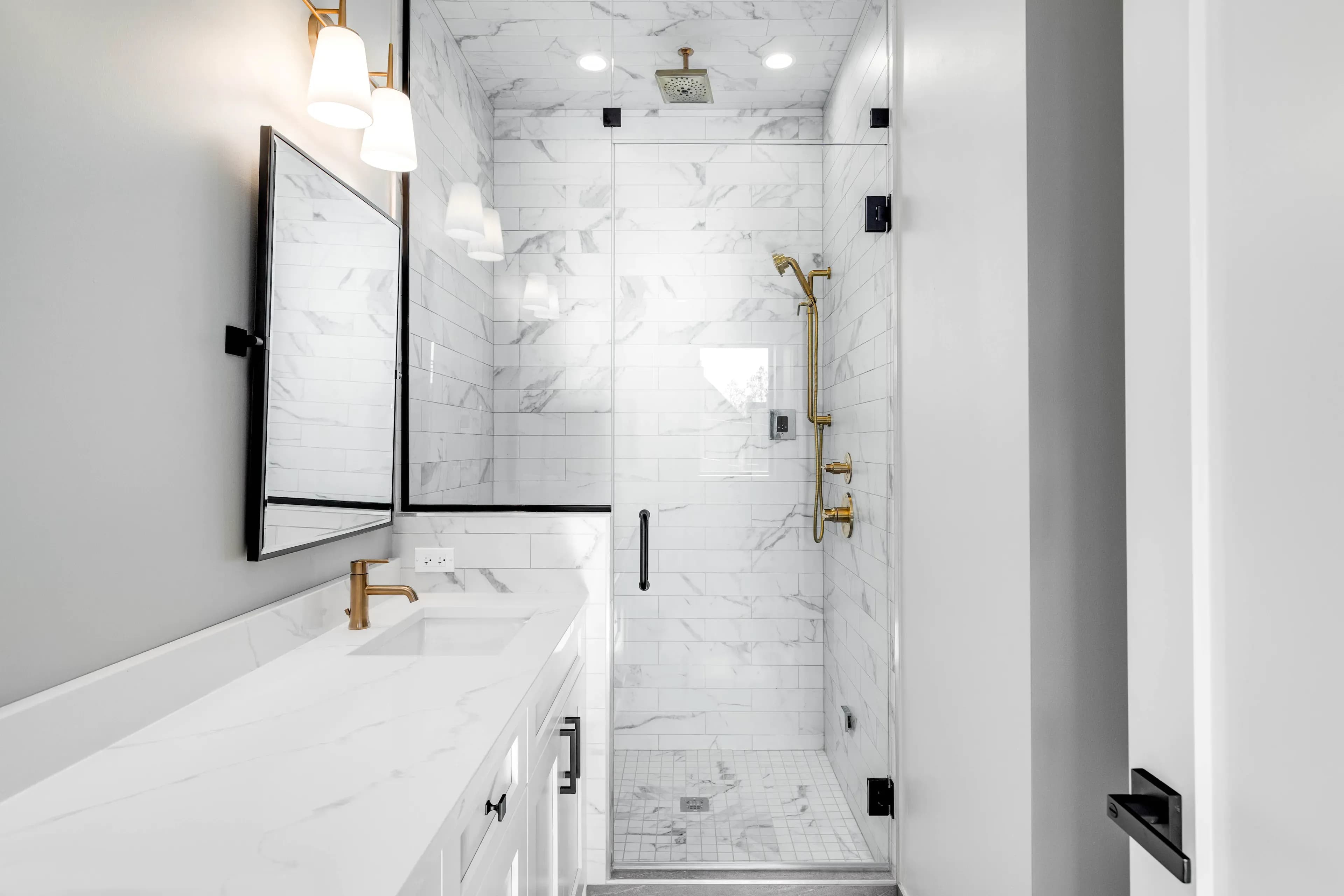 Small bathroom setting with glass shower doors. On one side, there's a sink and a rectangle mirror against white walls