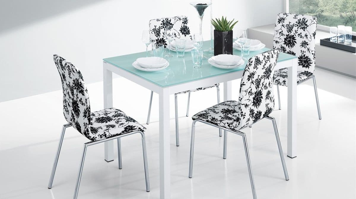 Modern dining table with a custom glass top, surrounded by stylish chairs featuring black and white floral patterns, showcasing contemporary design and elegance.