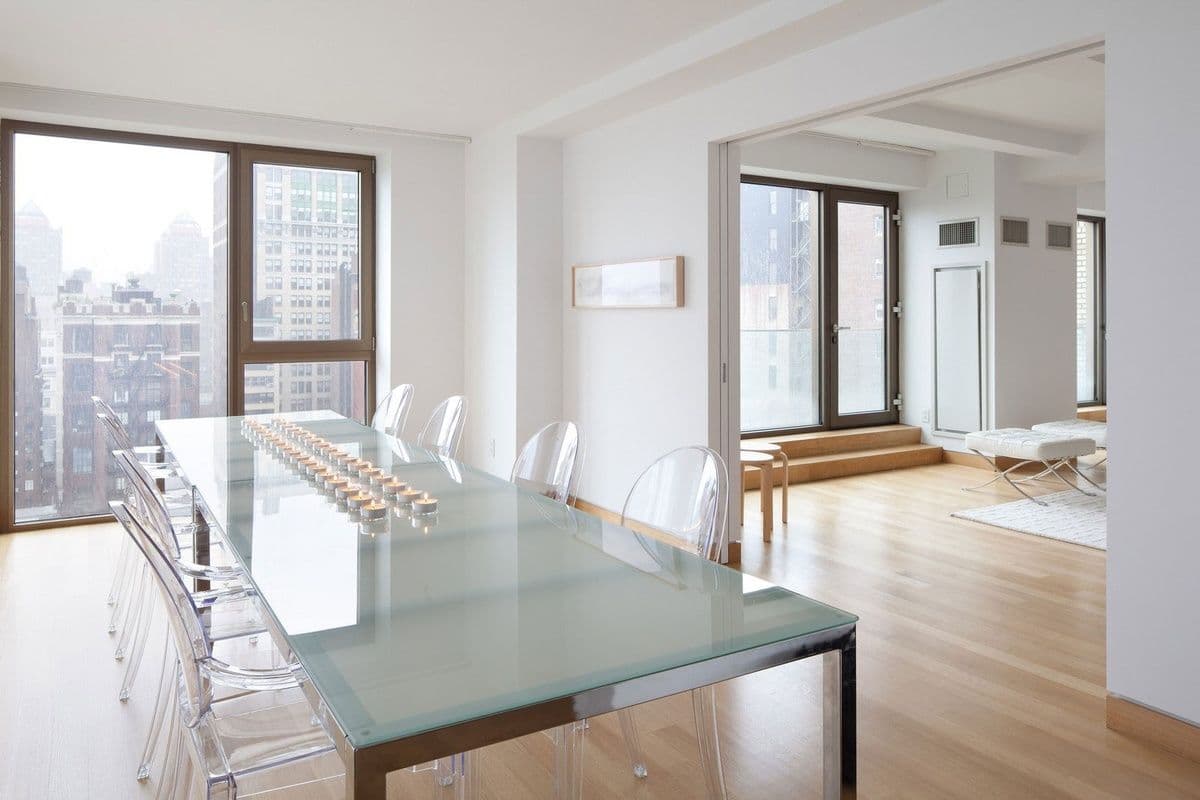 Modern dining room with a custom glass table top, featuring a sleek design and surrounded by transparent chairs, showcasing natural light and city views through large windows.