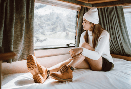 A woman sitting on a bed in a cozy environment with a view outside