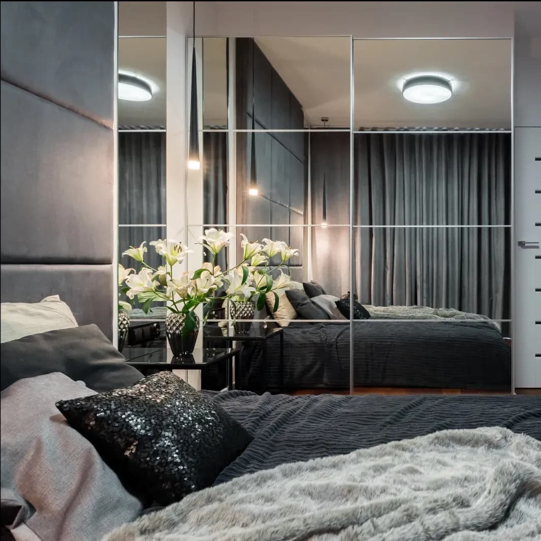 Modern bedroom featuring custom glass mirrors reflecting a stylish decor, complemented by sleek table tops and elegant textures, ideal for showcasing tempered and beveled glass edge designs.
