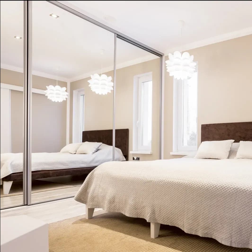 Modern bedroom featuring a custom glass mirror wardrobe, stylish light fixtures, and a cozy bed, highlighting the elegance of tempered glass designs.
