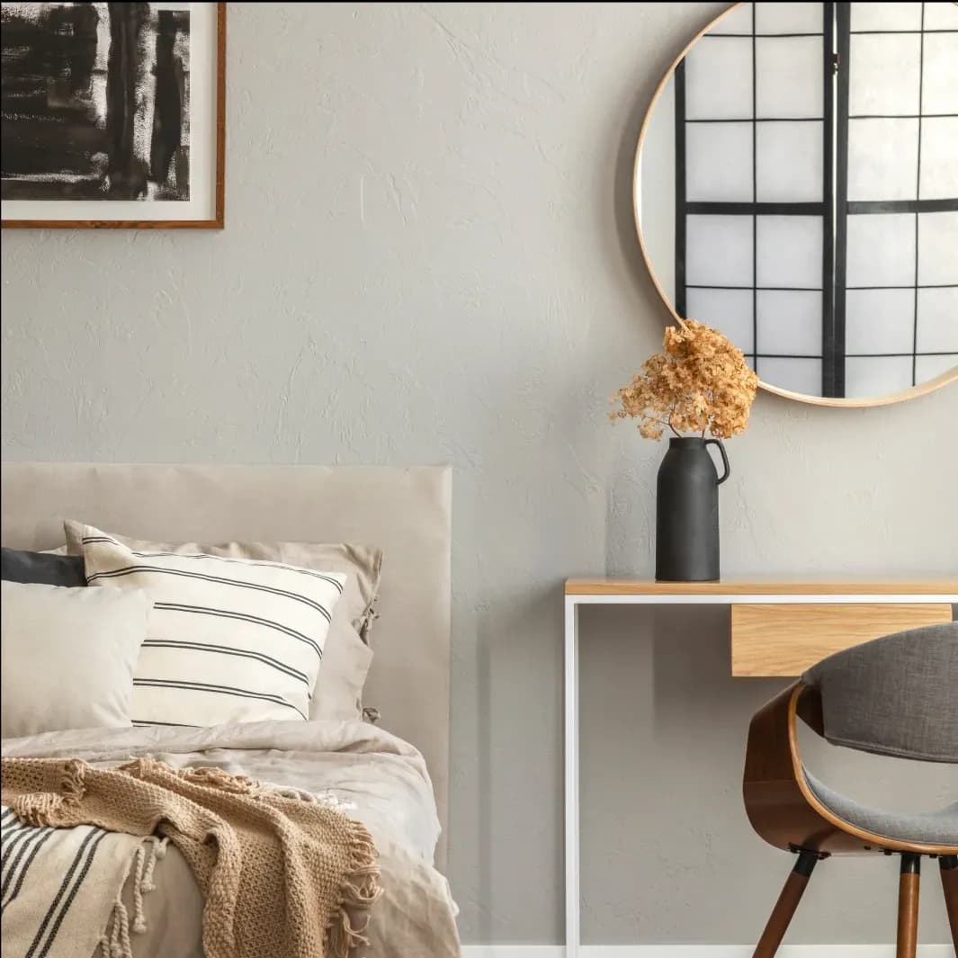Stylish bedroom interior featuring a round mirror with a beveled glass edge, modern table design, decorative vase, and cozy bedding, highlighting custom glass elements.
