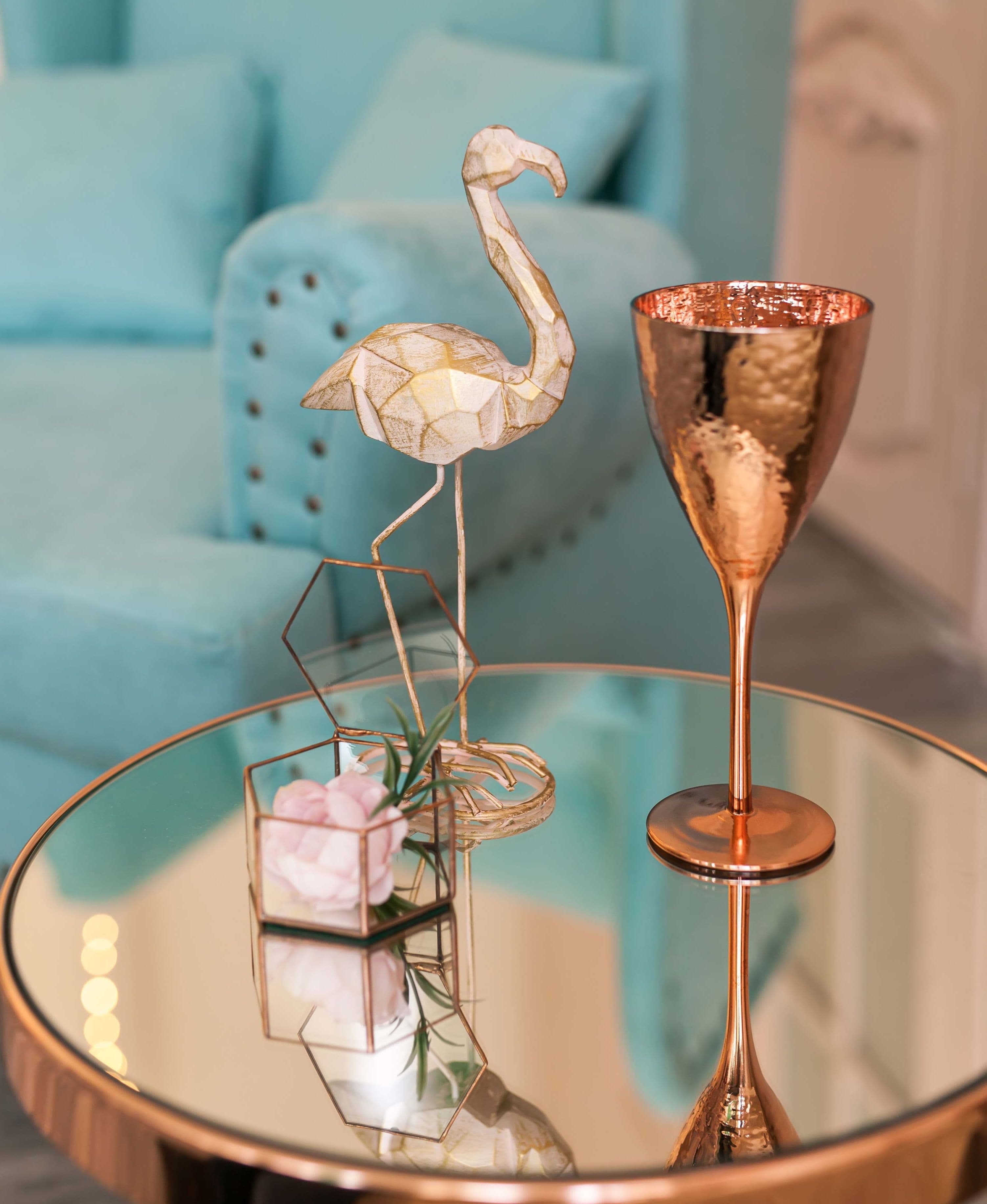 Reflective glass table top showcasing decorative elements like a flamingo figurine and a flower arrangement, emphasizing custom glass design and elegance.