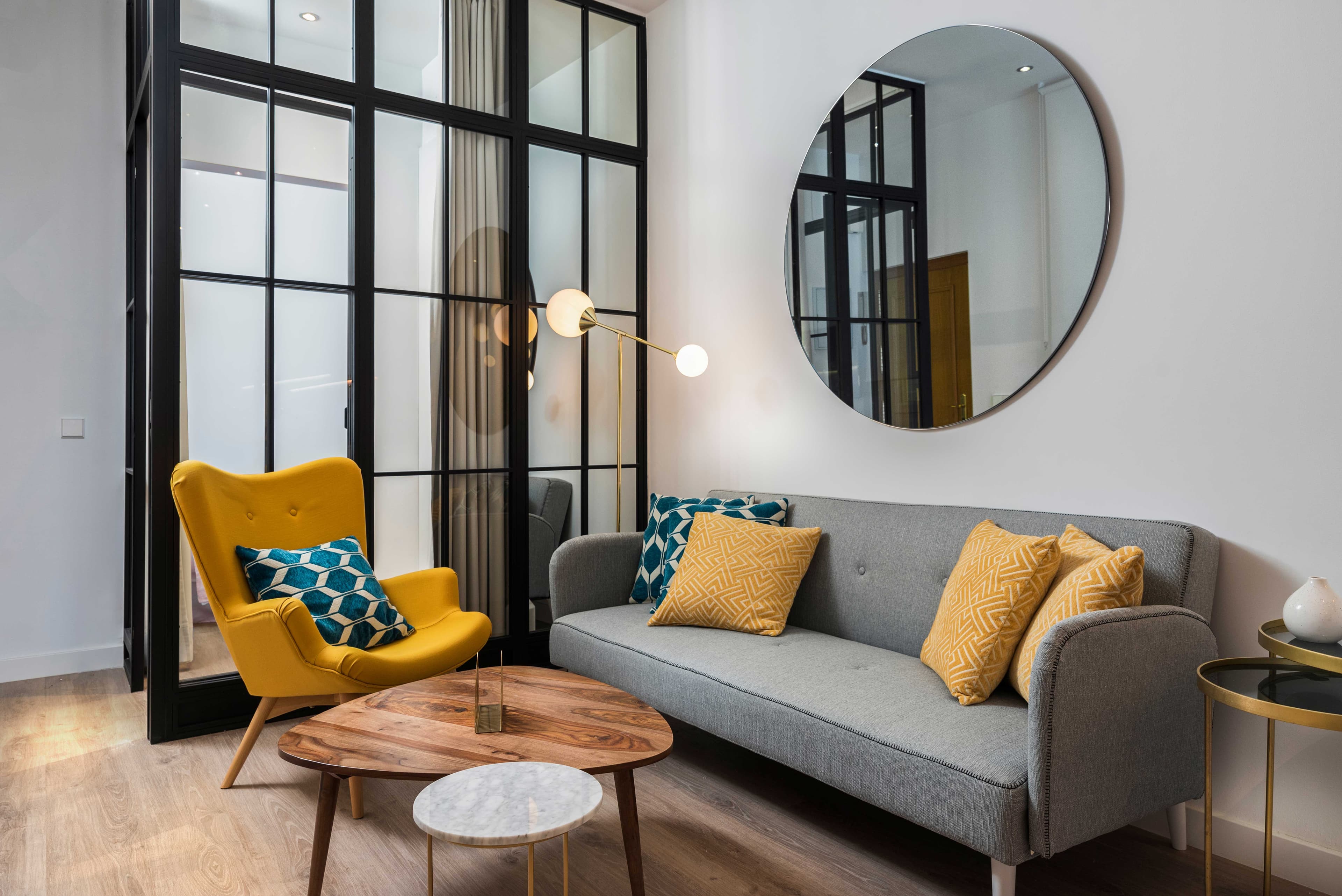 Modern living room featuring a round mirror, stylish furniture, and custom glass elements, highlighting tempered glass decor and a beveled glass edge.