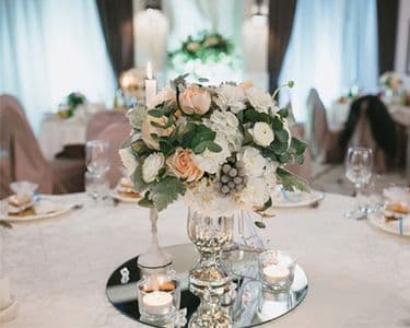 Elegant table centerpiece featuring fresh flowers and candles on a mirrored table top, showcasing custom glass design and beveled glass edge.