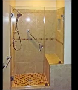 Custom glass shower doors with tempered glass in a modern tiled shower, featuring a seamless design and accessible seating area.