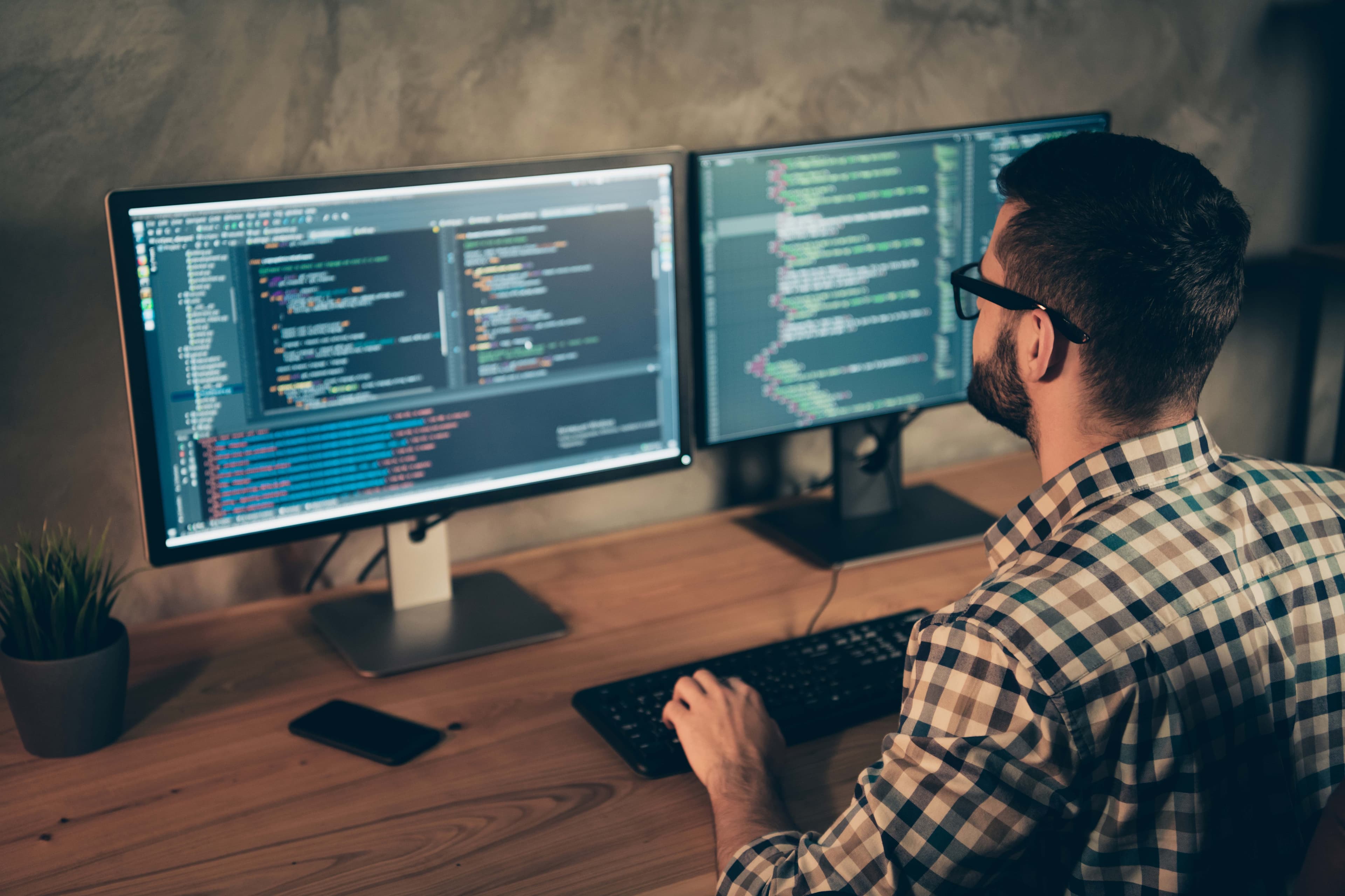 Professional working at dual monitors, focused on coding, with a modern workspace featuring custom glass elements like tempered glass and mirrors.