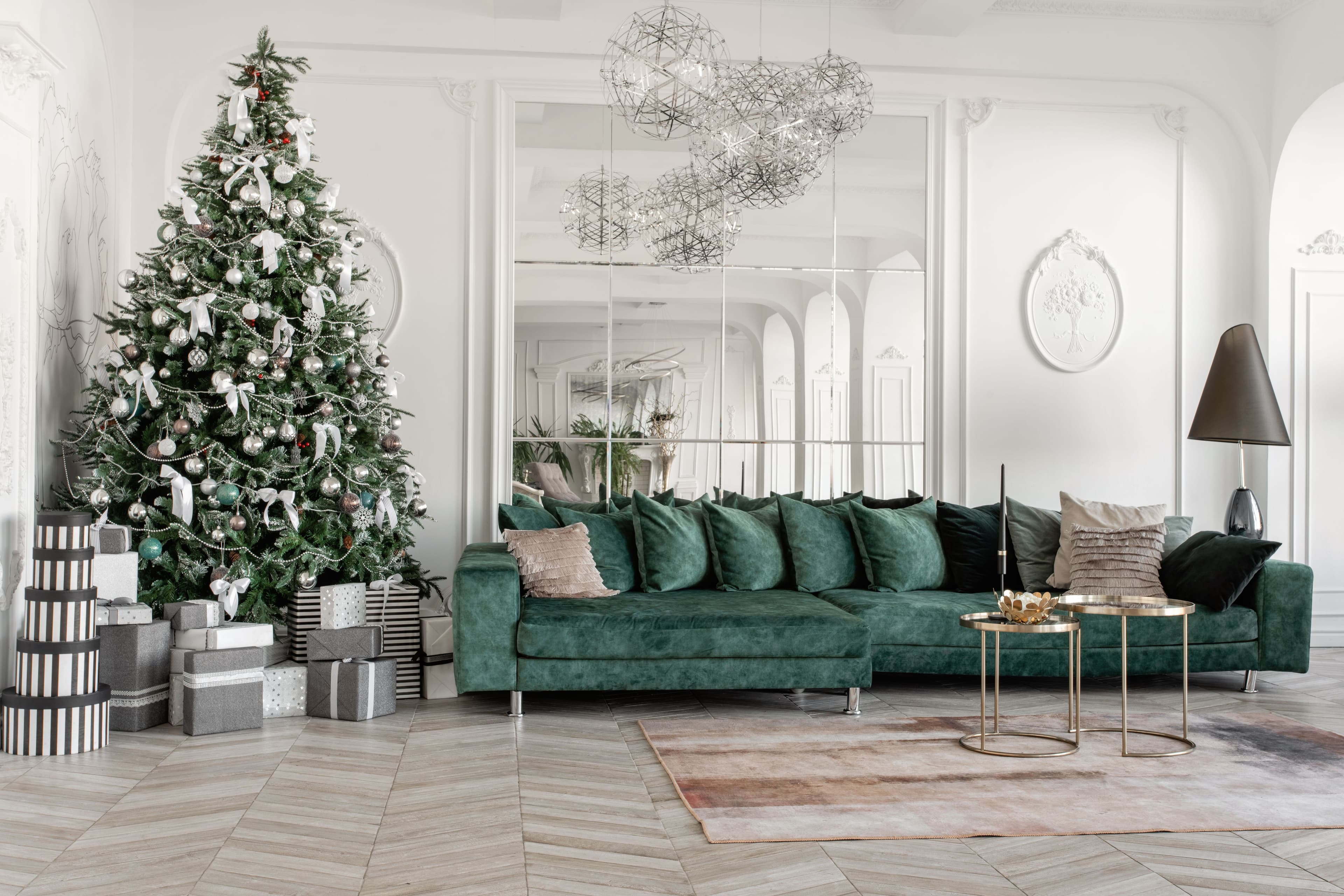 Modern living room with a green sectional sofa, decorated Christmas tree, custom mirrors, and stylish table tops, featuring a cozy atmosphere and elegant design elements.