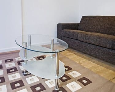 Modern living room featuring a custom glass coffee table with a tempered glass top, complemented by a cozy sofa and stylish rug, showcasing elegant design potential for glass products including shower doors and mirrors.
