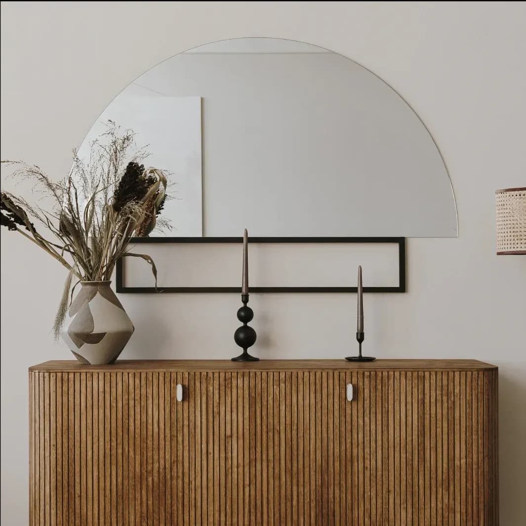 Custom beveled glass mirror above a wooden console table with decorative elements, featuring stylish candlesticks and a vase, highlighting the elegance of glass design in home decor.