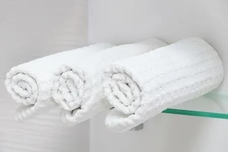 White rolled towels neatly placed on a glass shelf