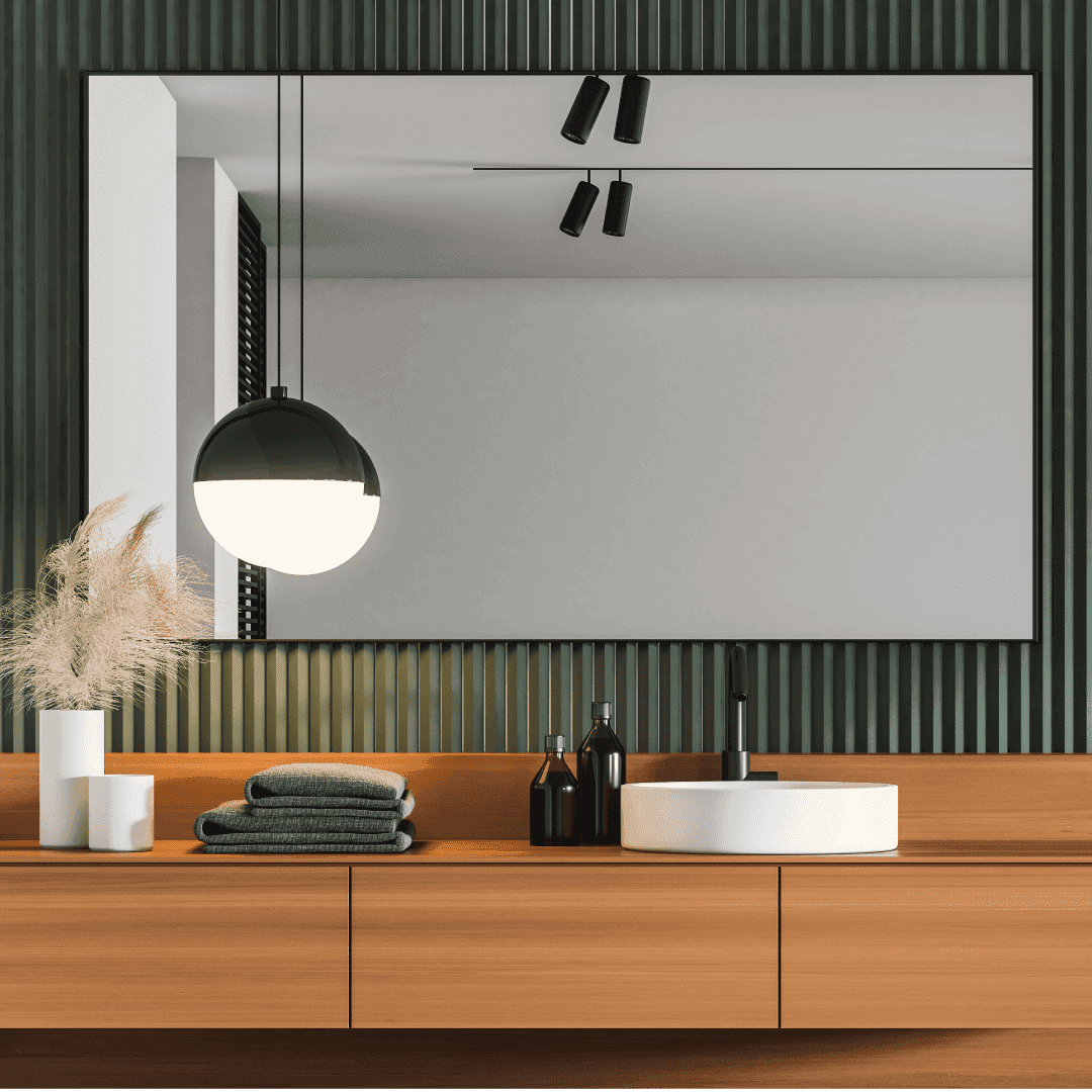 Modern bathroom featuring a large frameless mirror, stylish pendant light, and a wooden vanity with neatly arranged towels and decor, highlighting custom glass and contemporary design elements.