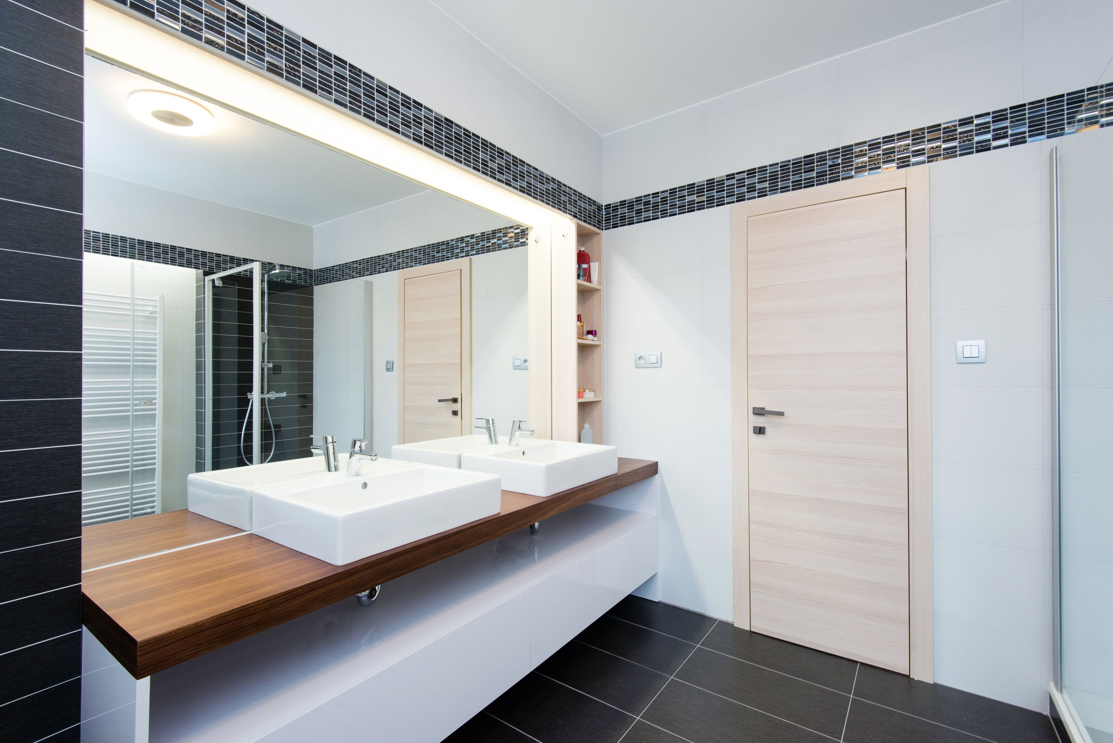 Modern bathroom featuring custom glass mirrors and shower doors, complemented by a stylish wooden countertop with vessel sinks.