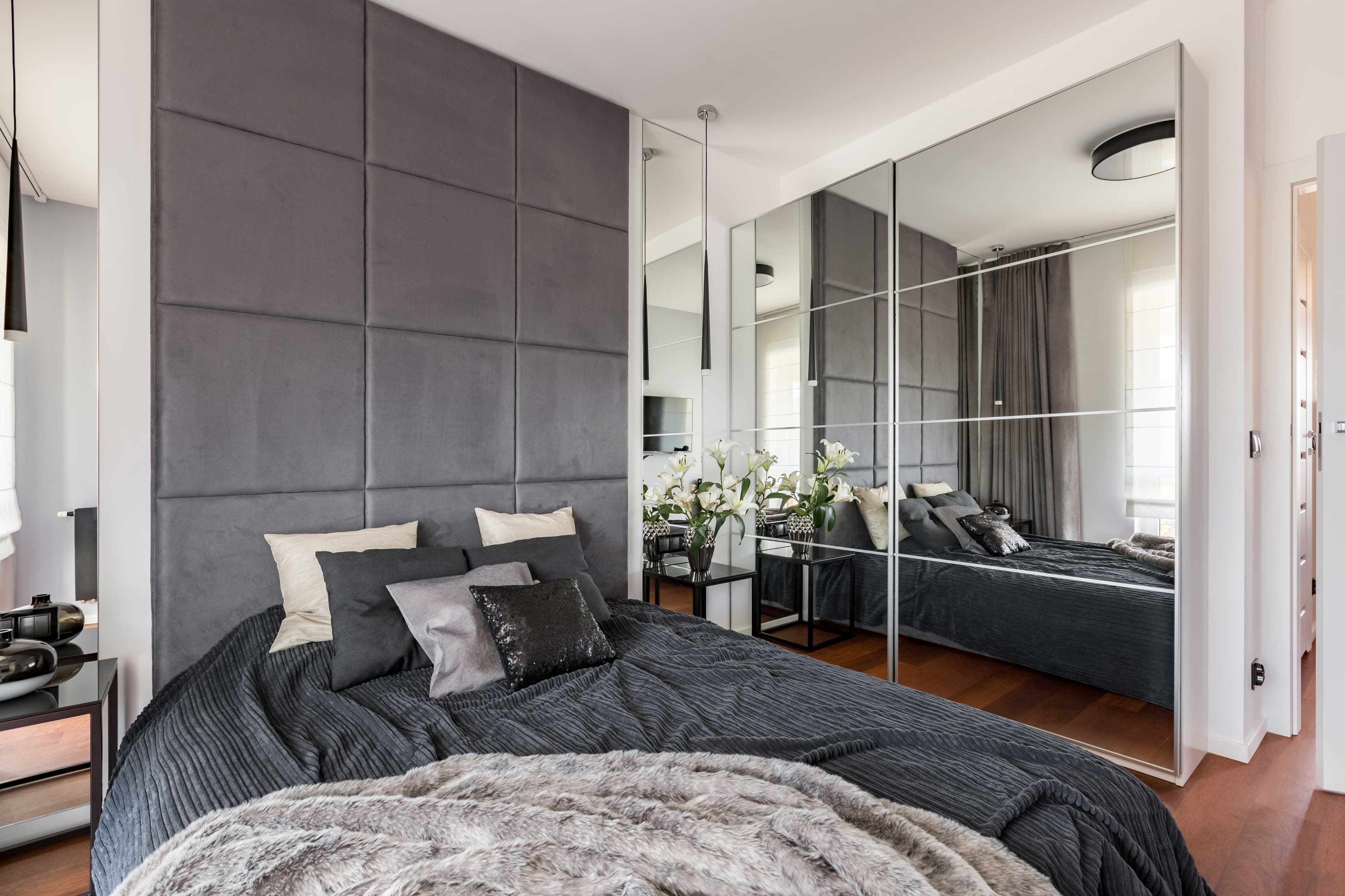 Modern bedroom featuring custom mirrors, dark bedding, and decorative pillows, highlighting custom glass design with tempered glass elements and beveled glass edges.