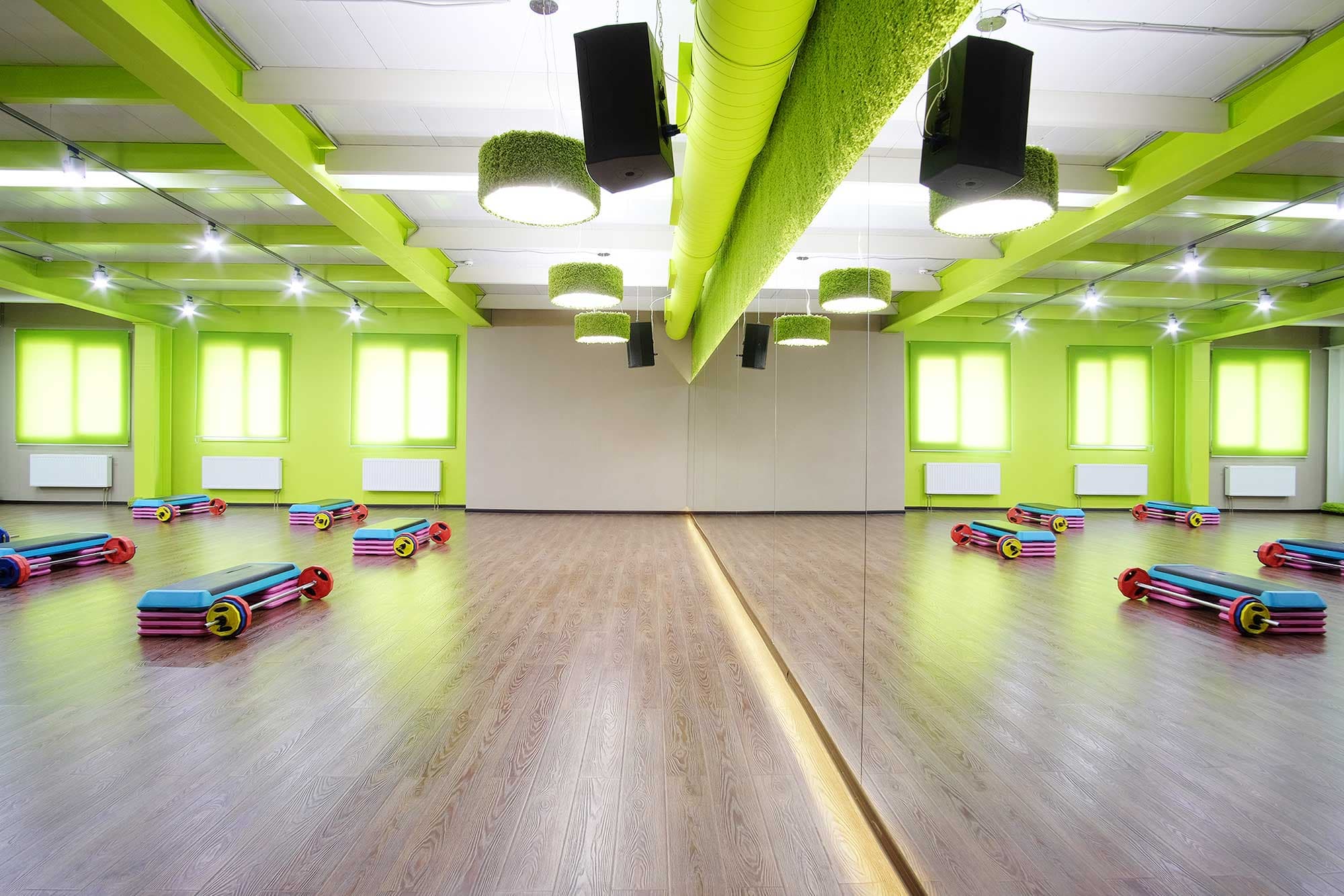 Bright fitness studio with large mirrors, colorful exercise mats, and green accents, showcasing custom glass solutions and mirrored surfaces ideal for shower doors and table tops.