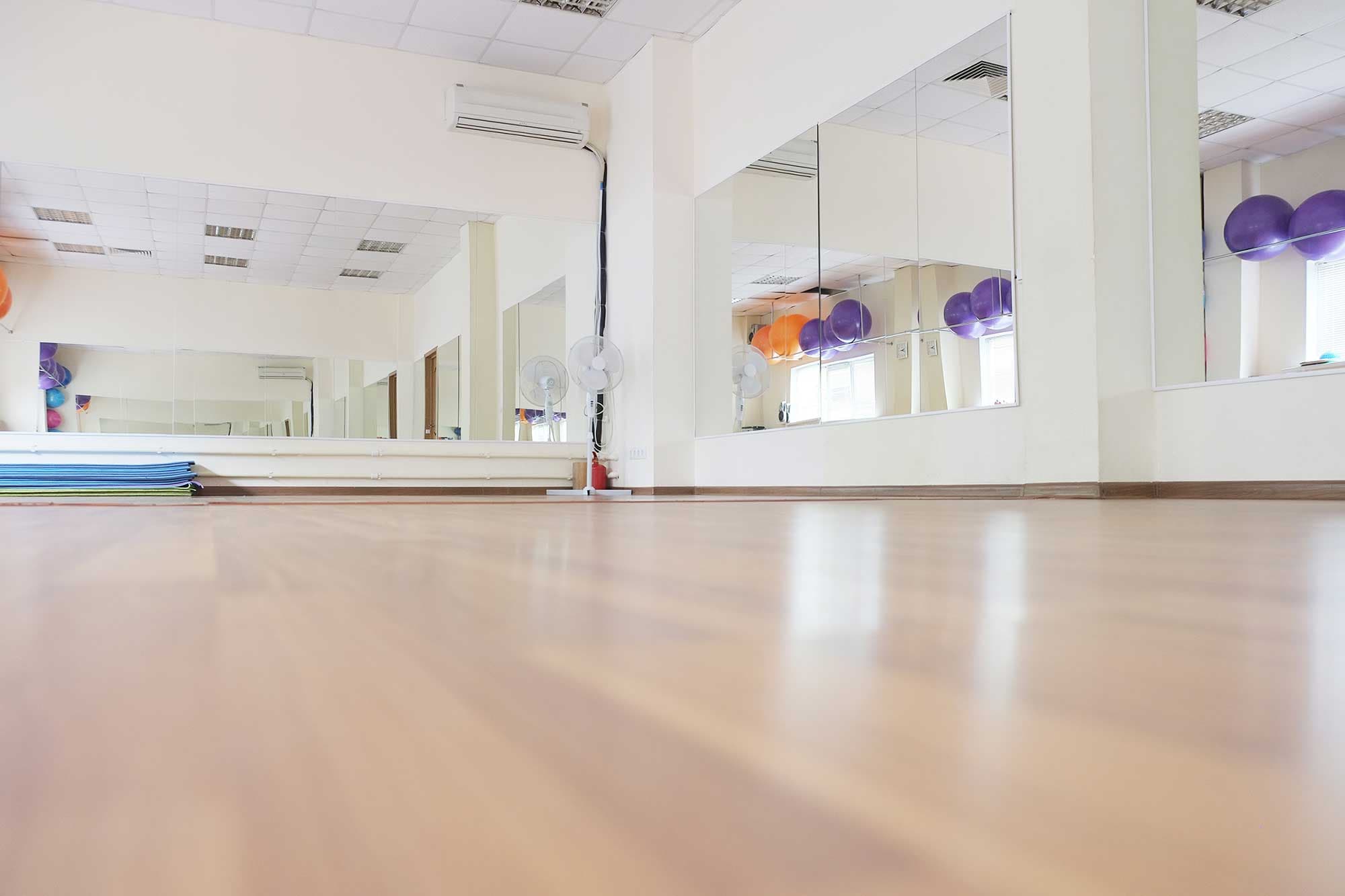 Large mirrors reflecting a bright room with wooden flooring, showcasing custom glass installations perfect for studios, gyms, or fitness centers.