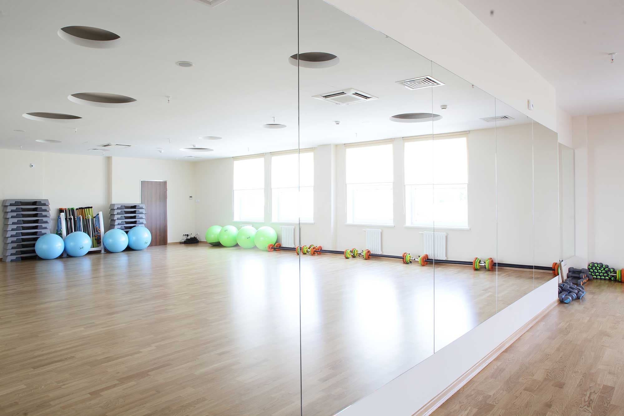 Large custom mirror on wall in fitness studio, showcasing lively gym equipment and bright space, ideal for shower doors, table tops, and tempered glass solutions.