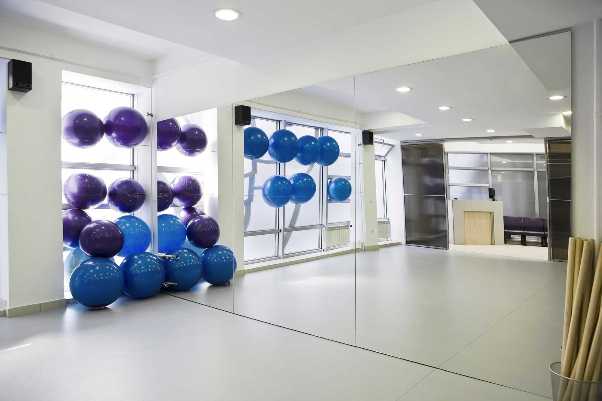 Modern exercise studio featuring custom mirrors and colorful exercise balls, highlighting spacious design and functionality with an emphasis on glass solutions like tempered and beveled edges.