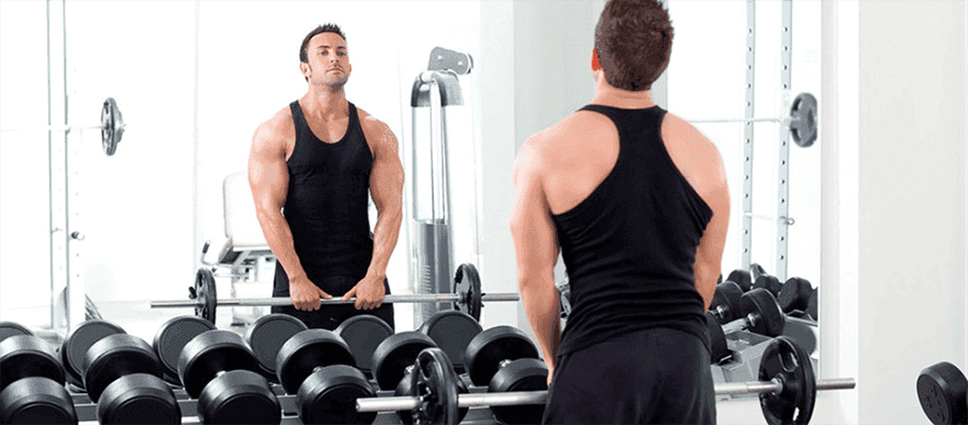 Man lifting weights in a gym with a mirrored wall