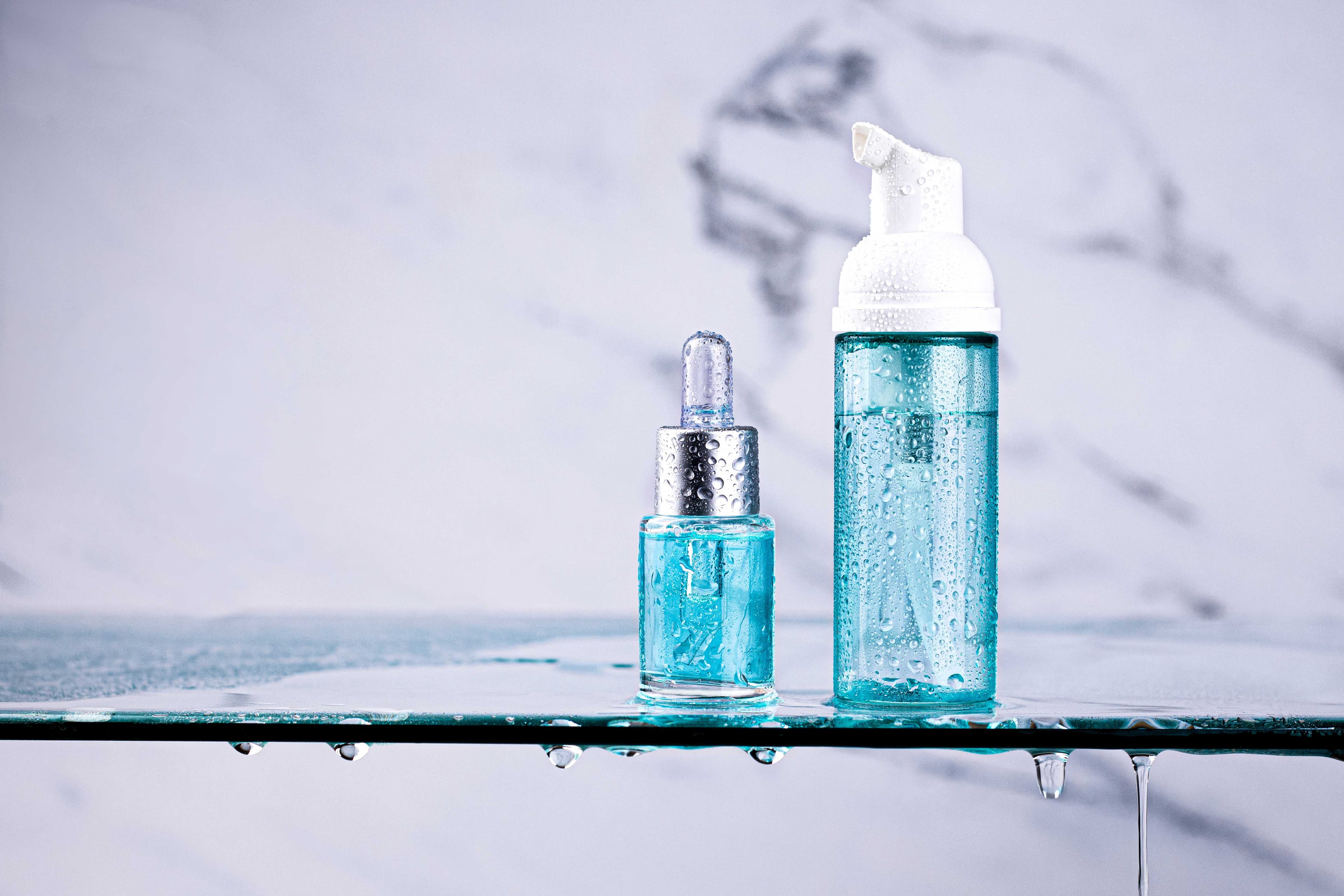 Custom glass tabletop featuring water droplets, with skincare bottles reflecting a modern aesthetic, showcasing our expert design in shower doors, mirrors, and tempered glass edges.