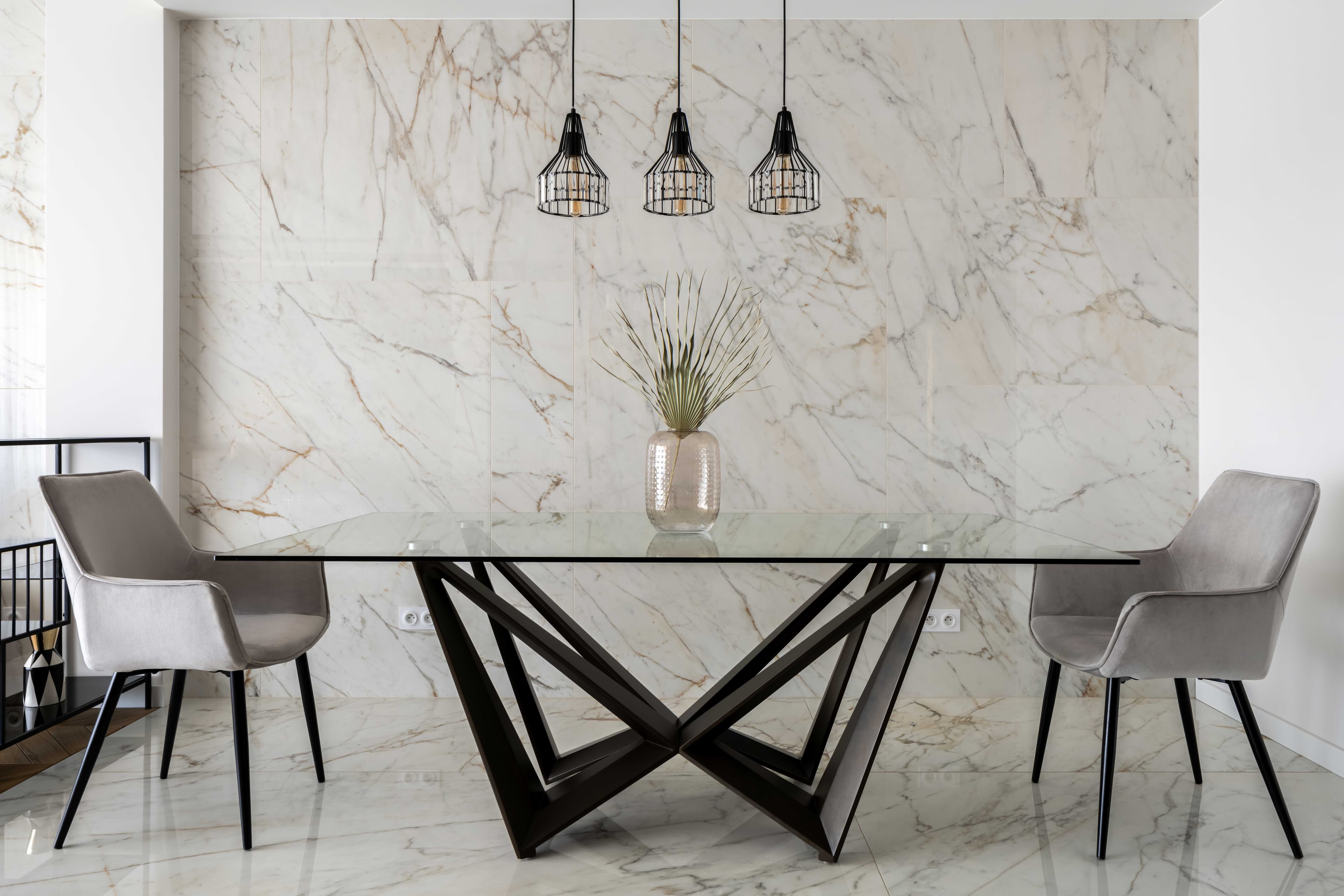 Modern dining table with a custom glass top, featuring a unique black base and surrounded by stylish chairs, set against a marble wall, ideal for showcasing tempered and beveled glass designs.