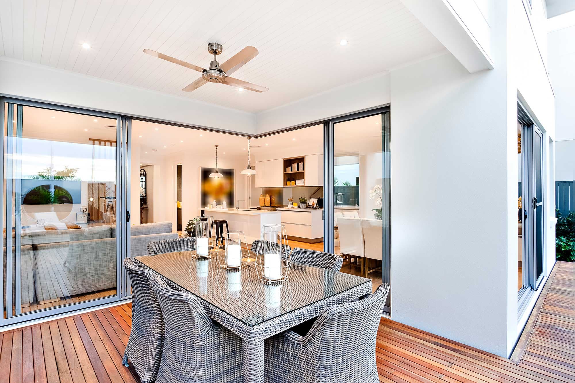 Modern outdoor dining area featuring a glass table top, surrounded by wicker chairs, with tempered glass sliding doors leading to the interior, showcasing custom glass design elements.