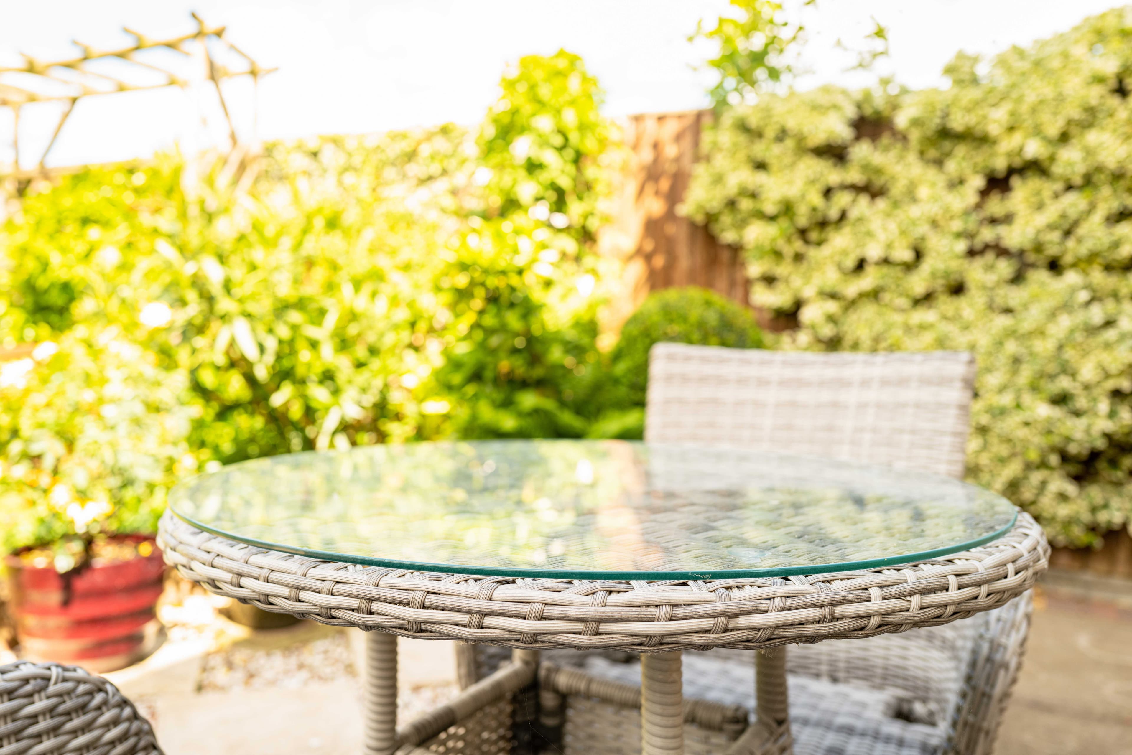 Custom round glass table top with beveled edges on a wicker patio table, surrounded by greenery. Ideal for showcasing tempered glass options.