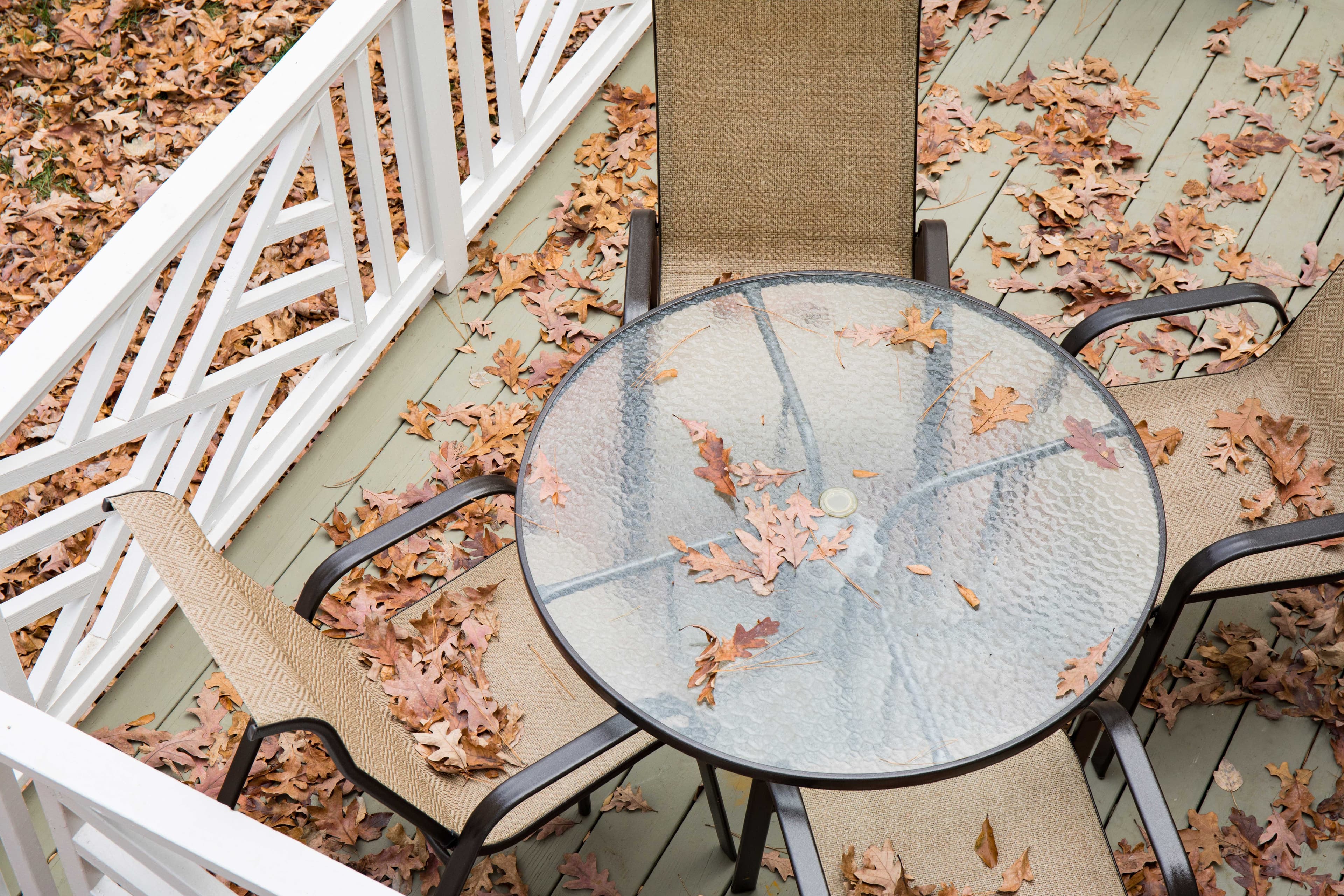 A round glass table surrounded by chairs, covered with autumn leaves, showcasing custom glass design and textured tempered glass surface.