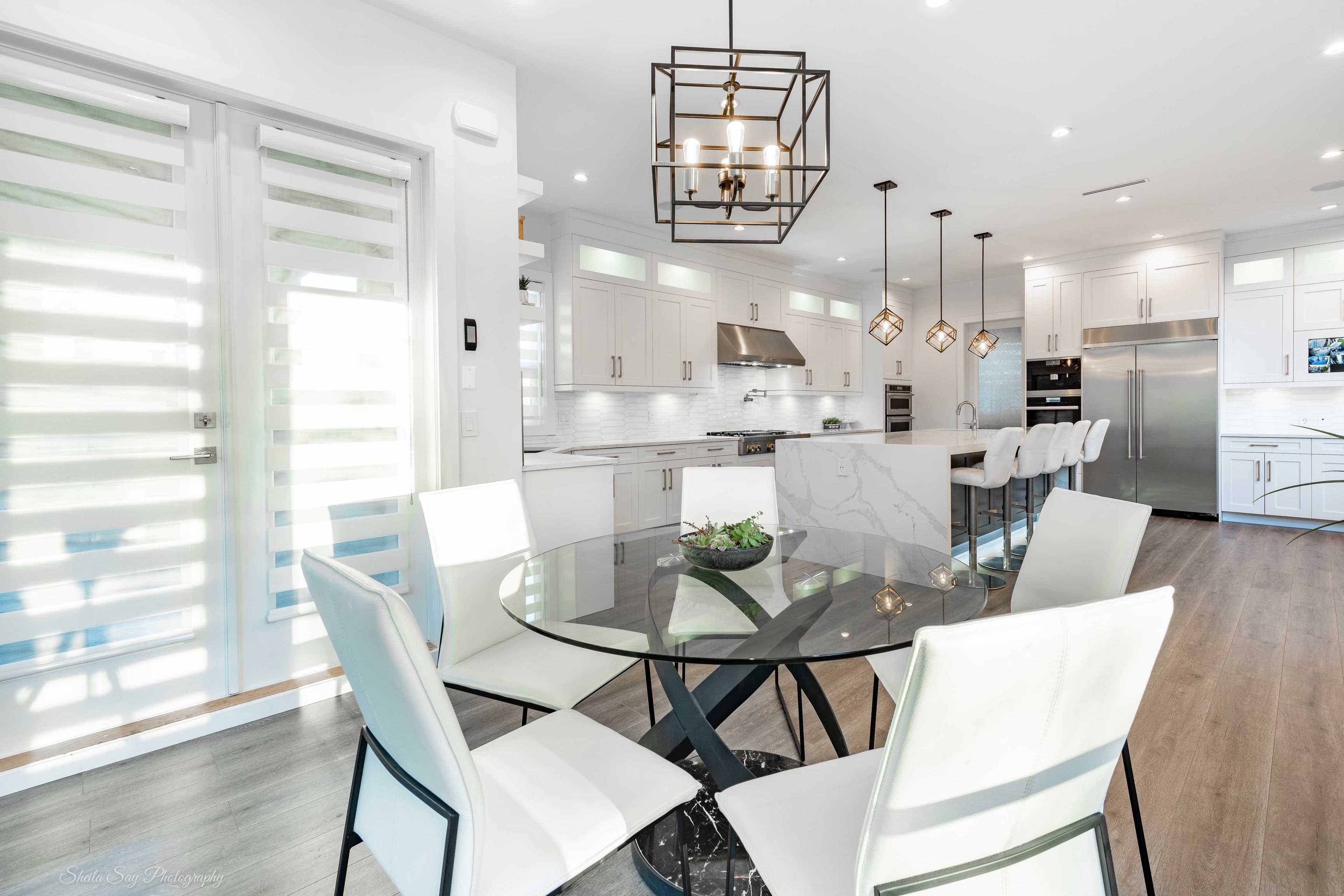 modern kitchen featuring a round glass table with a beveled edge, stylish white chairs, and custom cabinetry illuminated by contemporary lighting fixtures, showcasing the elegance of custom glass designs.