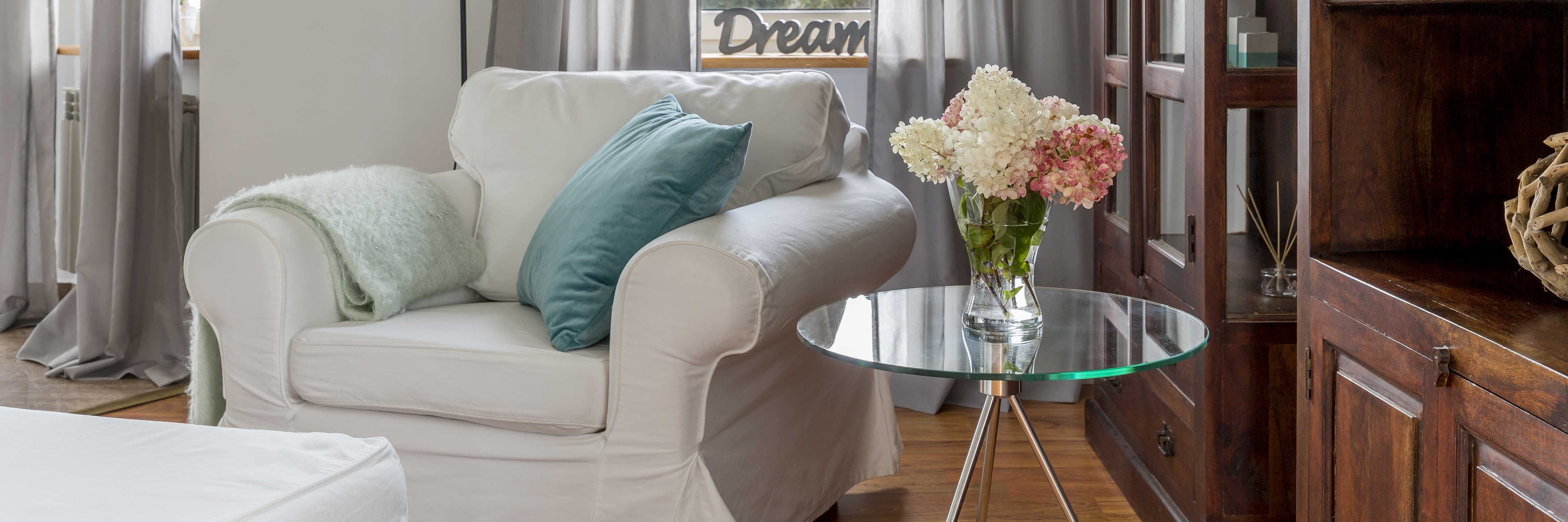 cozy living room with a white couch, decorative pillows, and a glass side table showcasing a floral arrangement, highlighting the elegance of custom glass and tempered glass products in home decor