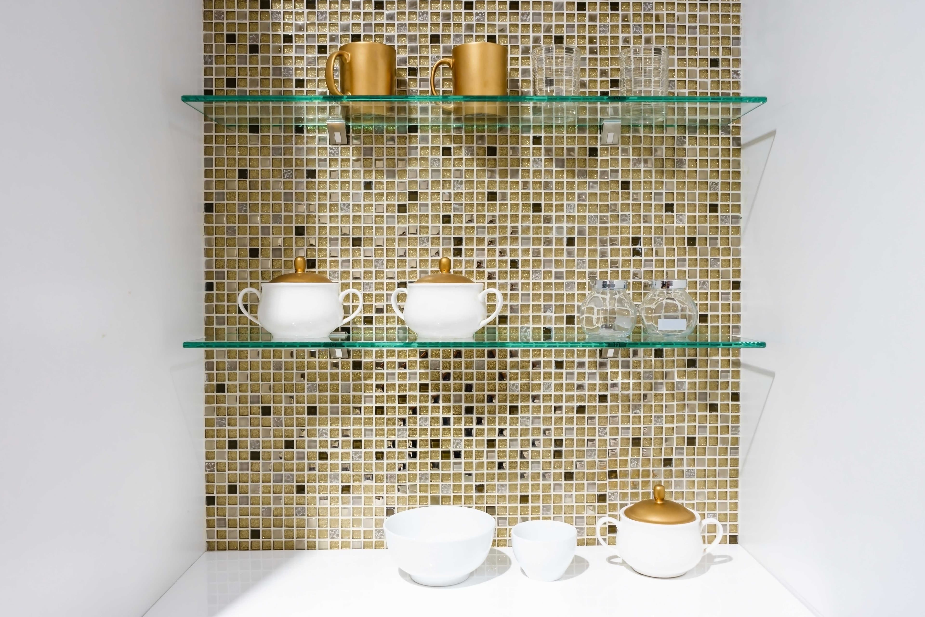Custom glass shelves displaying white and gold tableware, featuring tempered glass and a modern mosaic background, ideal for interior design.