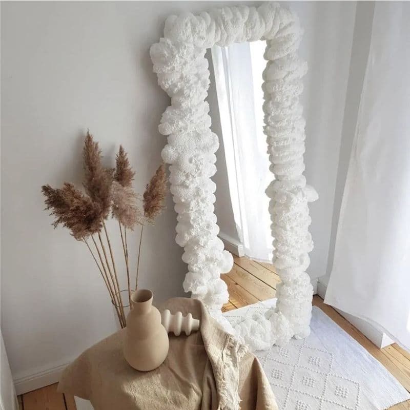 Decorative mirror with textured white frame, featuring elegant plants and minimalistic decor, showcasing custom glass artistry suitable for home design, including mirrors and tempered glass options.