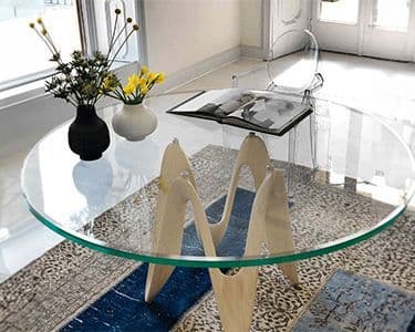 Custom glass table top with a beveled glass edge, showcasing a modern design in a stylish interior setting, complemented by decorative plants and a magazine.