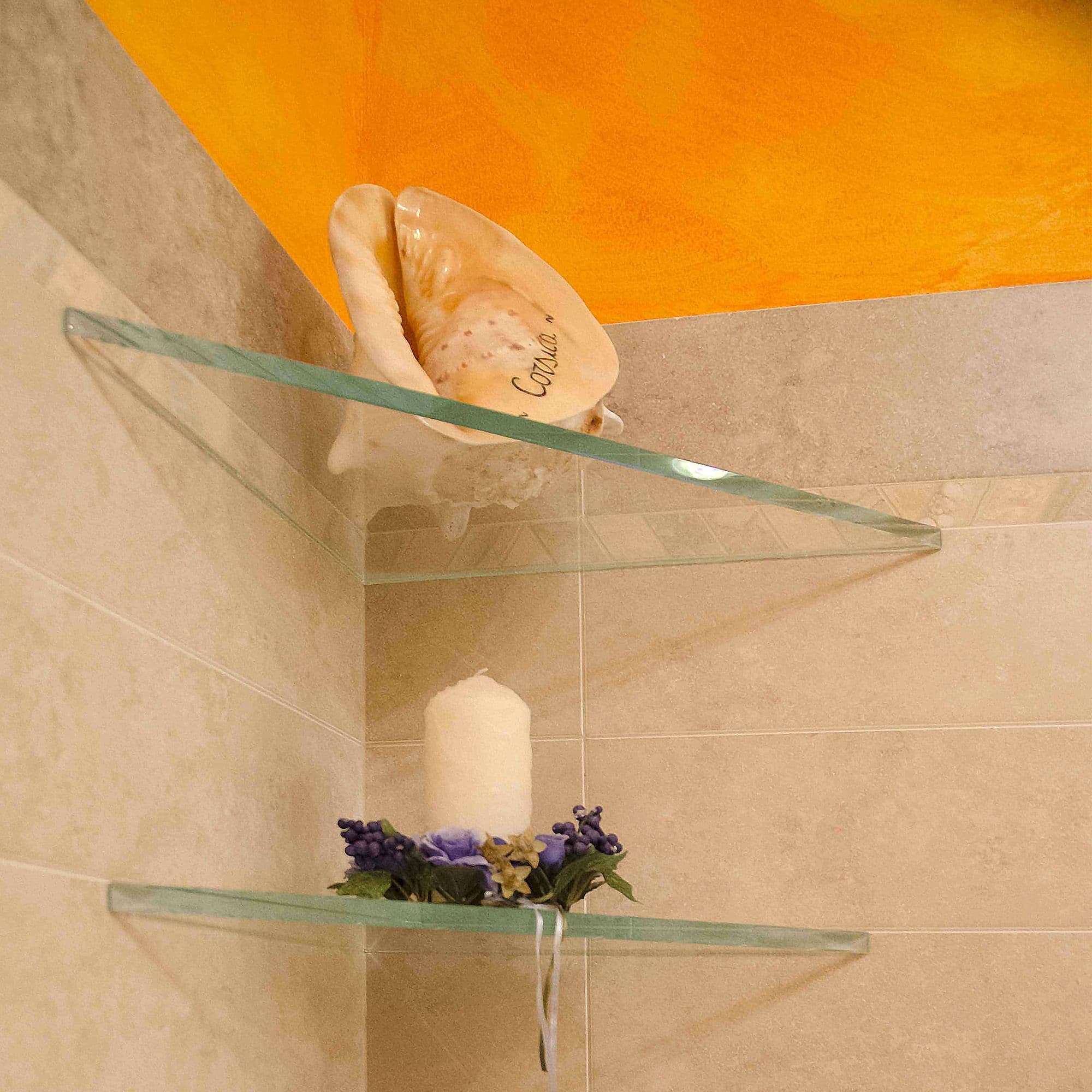 Custom glass shelves in a bathroom corner holding decorative items, showcasing tempered glass and beveled glass edge design, ideal for shower doors and table tops.