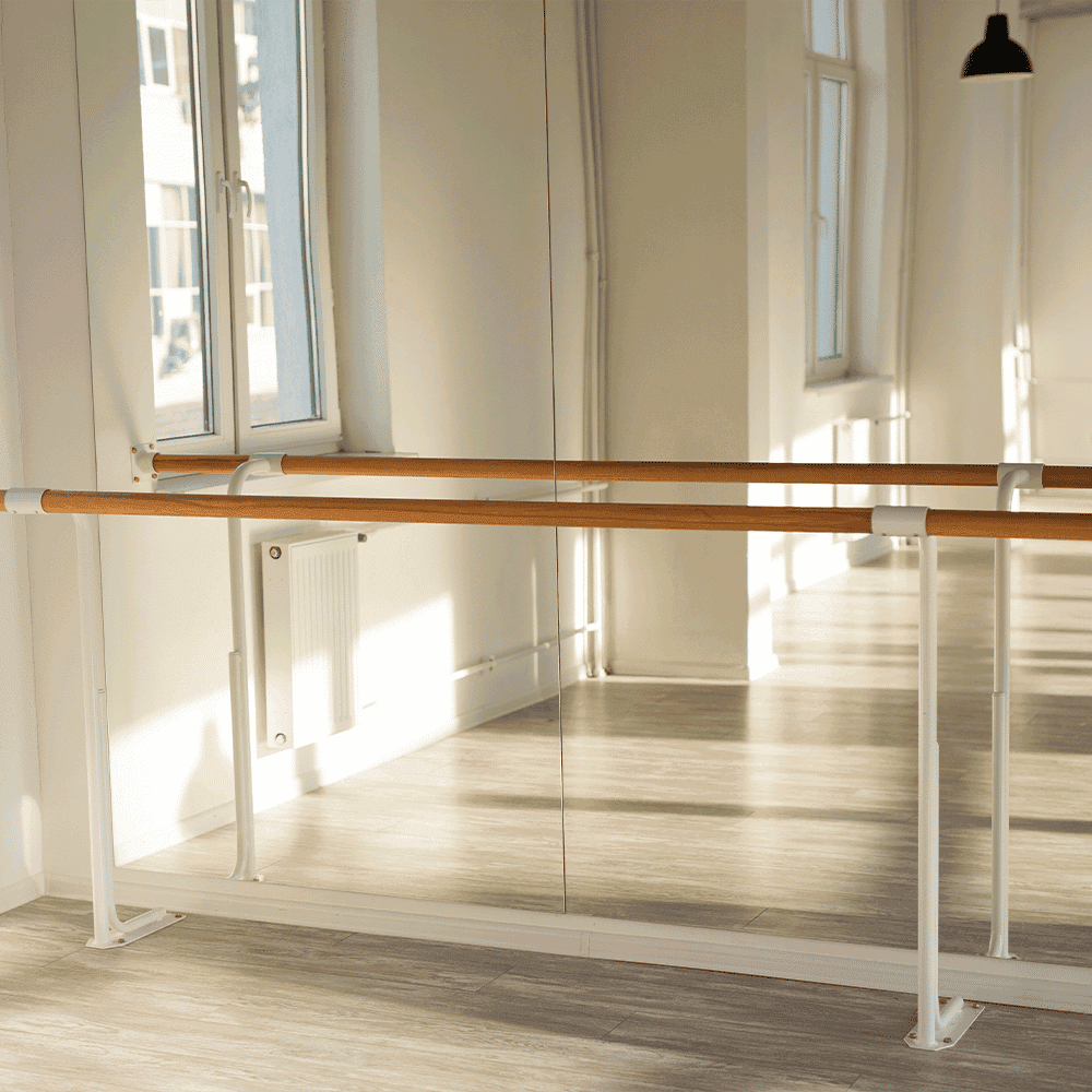 Custom glass mirror with a wooden ballet bar in a dance studio, featuring a spacious, well-lit interior ideal for showcasing shower doors, table tops, and tempered glass designs.