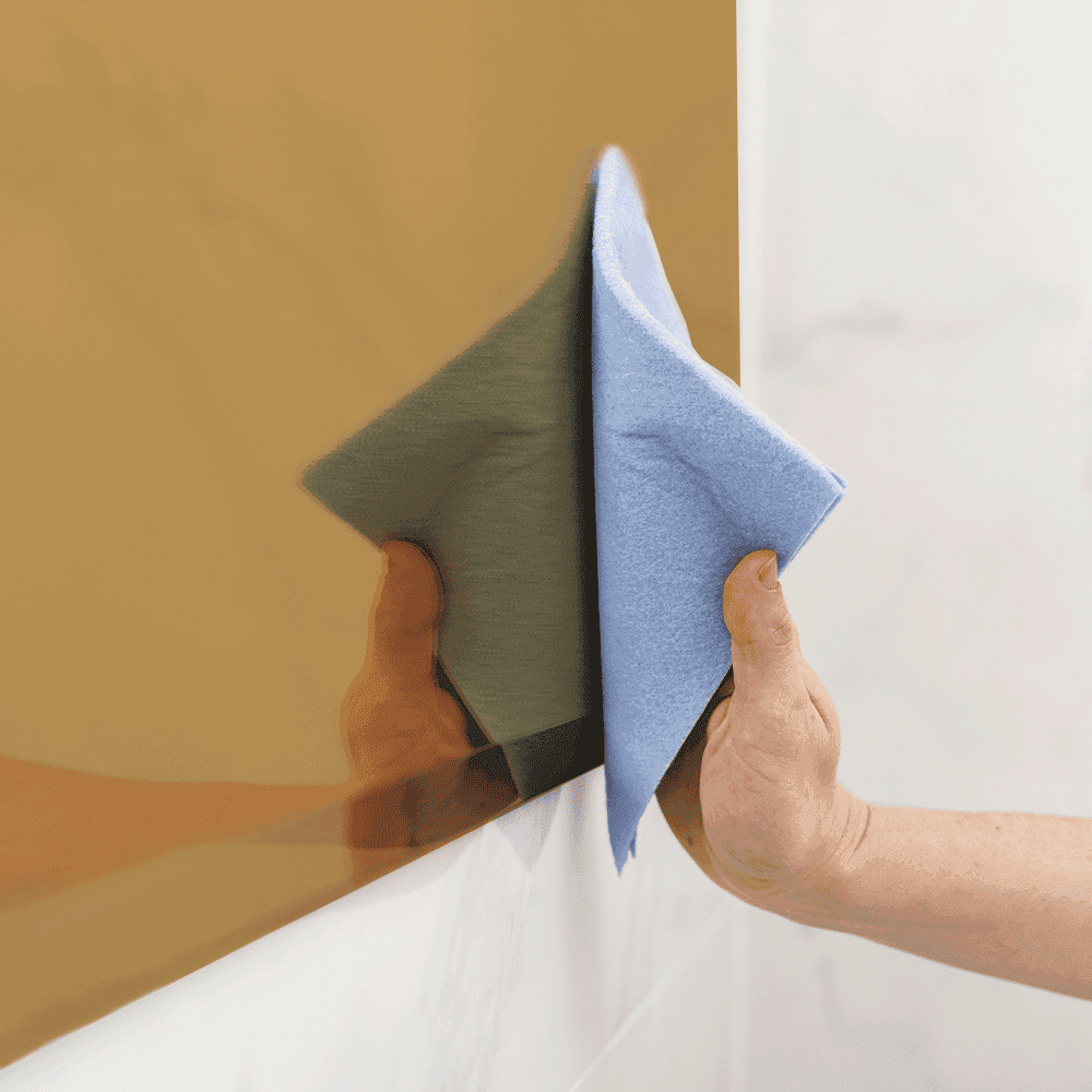 Person cleaning a custom glass mirror with a microfiber cloth, showcasing maintenance for shower doors, table tops, tempered glass, and beveled glass edges.