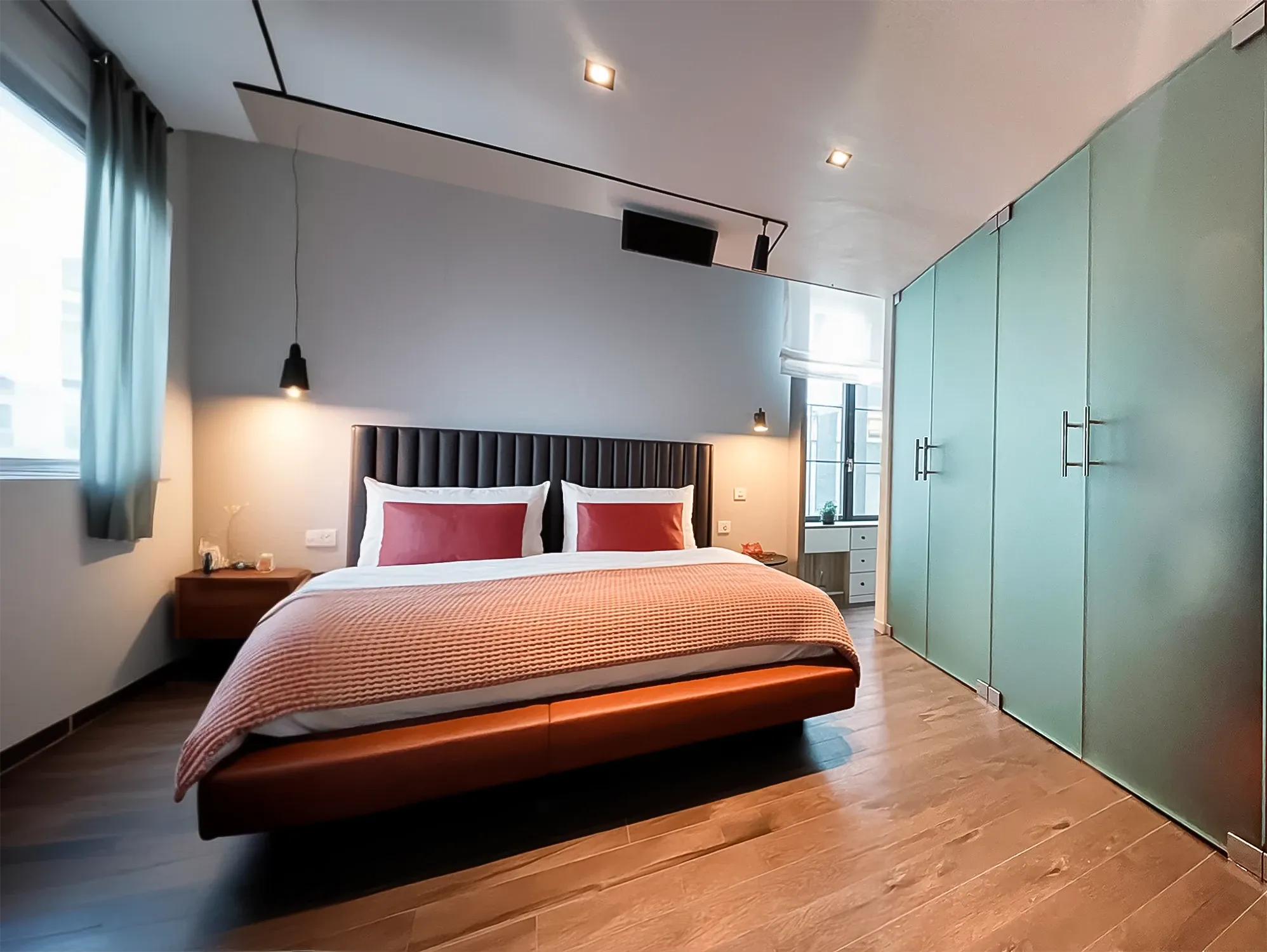 Modern bedroom featuring a leather bed with a tufted headboard and a floor-to-ceiling wardrobe with frosted glass doors.