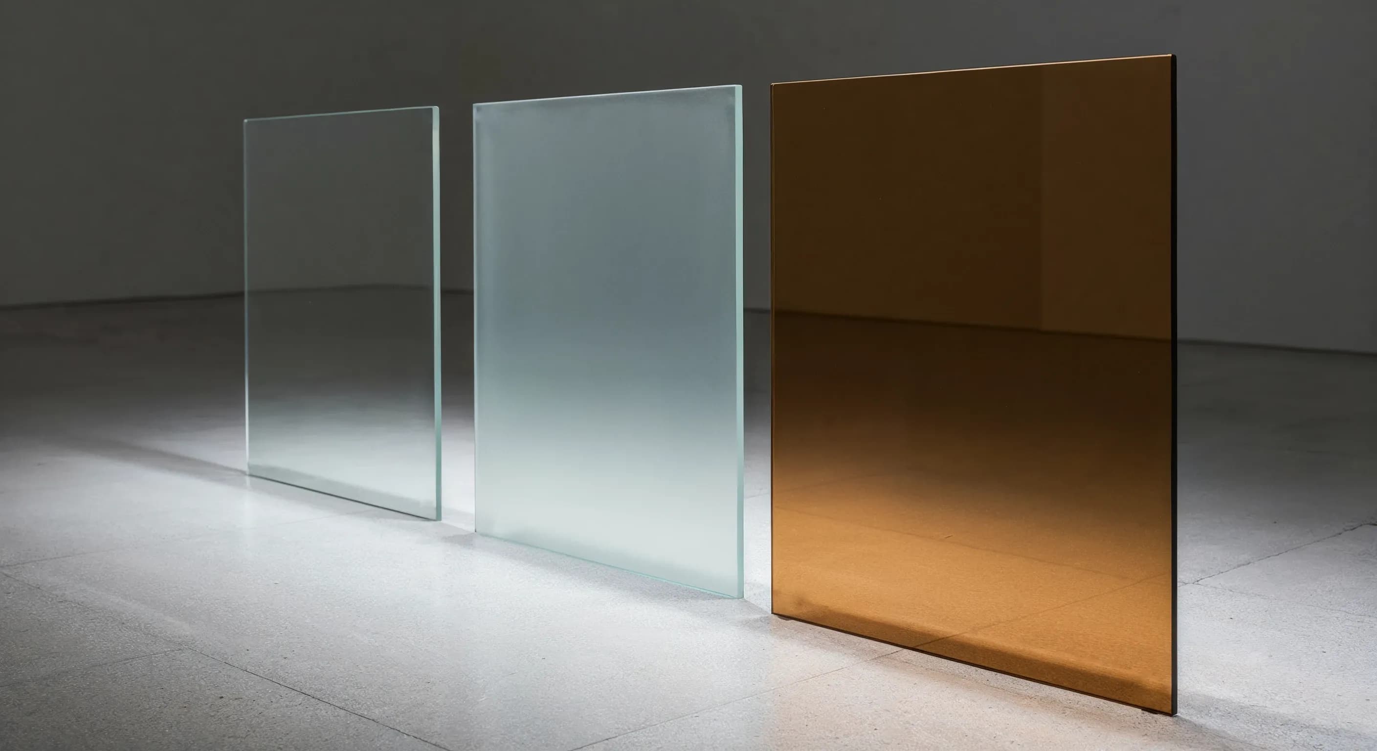 Three large glass panels showcasing different finishes, from left to right: standard clear glass, frosted acid-etched glass, and tinted bronze glass.