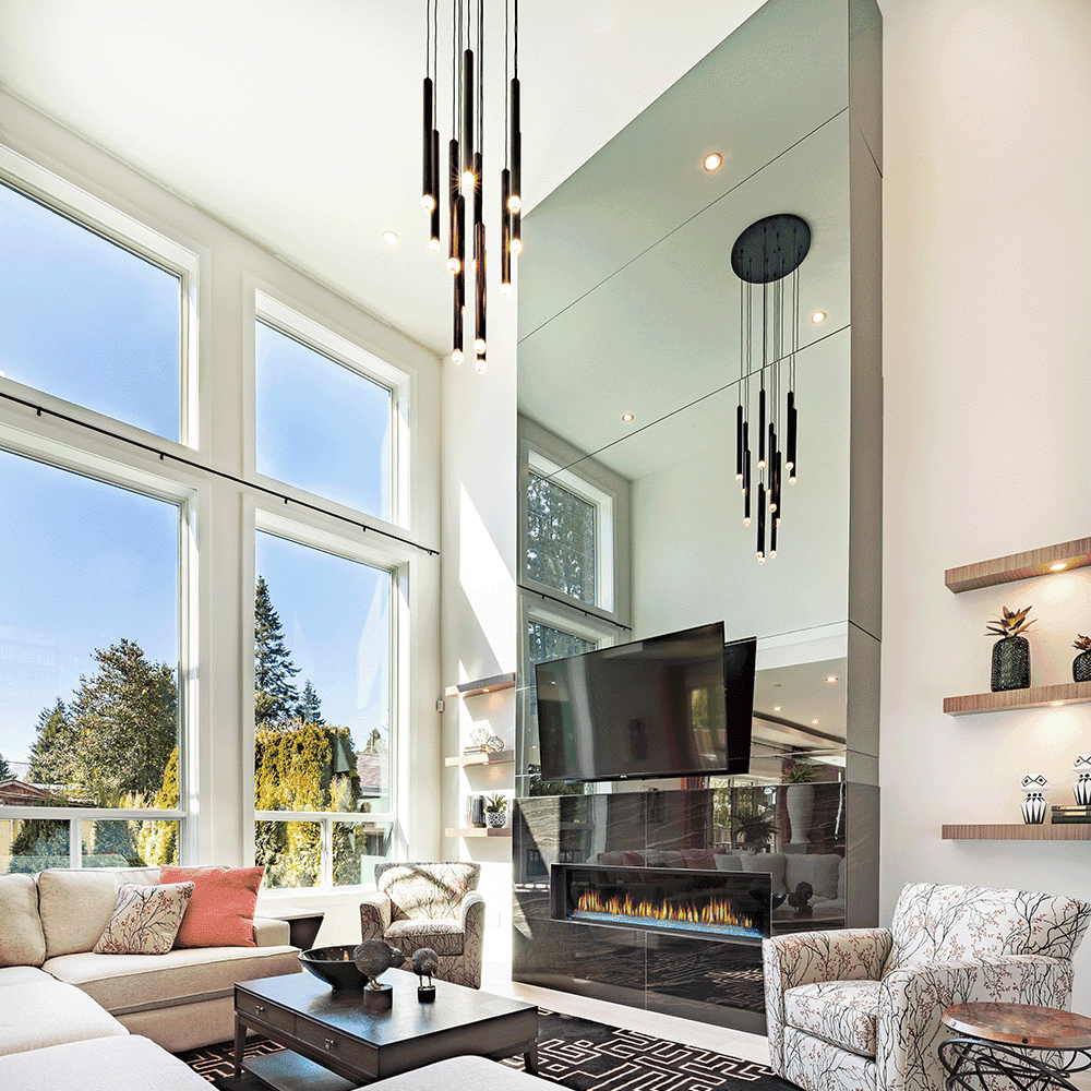 Modern living room featuring large windows, stylish pendant lighting, and a prominent wall mirror reflecting a cozy fireplace, showcasing custom glass design elements for an elegant aesthetic.