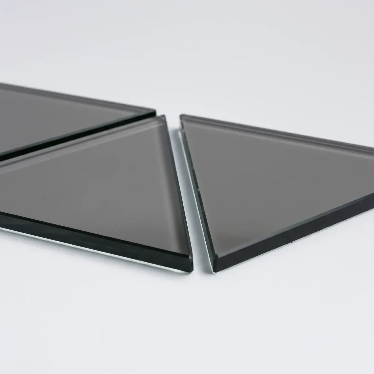 Three custom-cut, triangular pieces of sleek, grey-tinted glass with polished edges, arranged on a white surface.